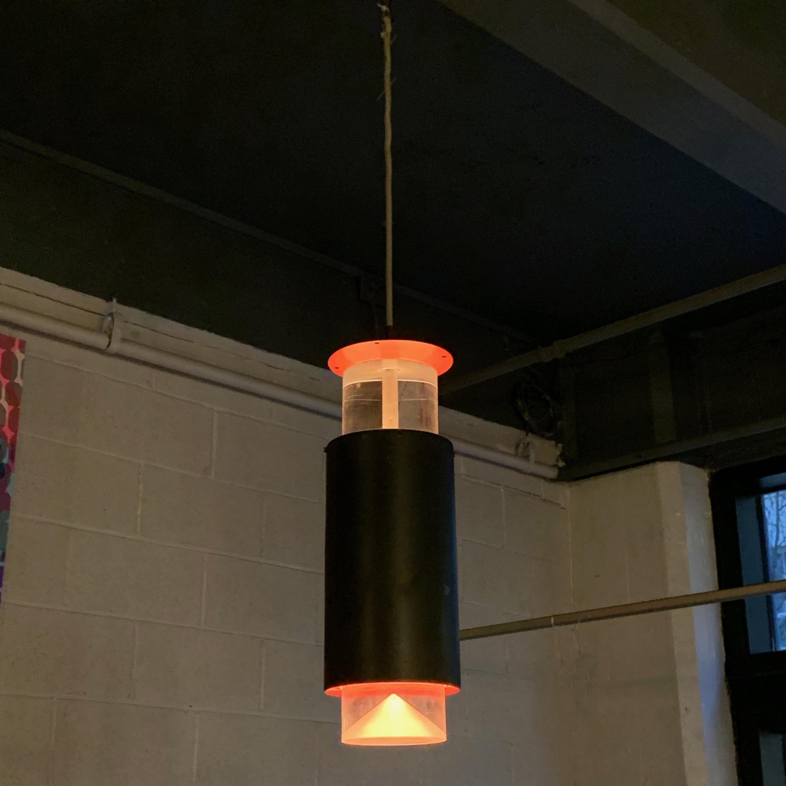 Danish modern, cylinder pendant light by Simon Henningsen plays with color and shadow to create a minimal, modernist feel. The light features suspended Lucite bands at top and bottom with black painted aluminum exterior band. The interior band and