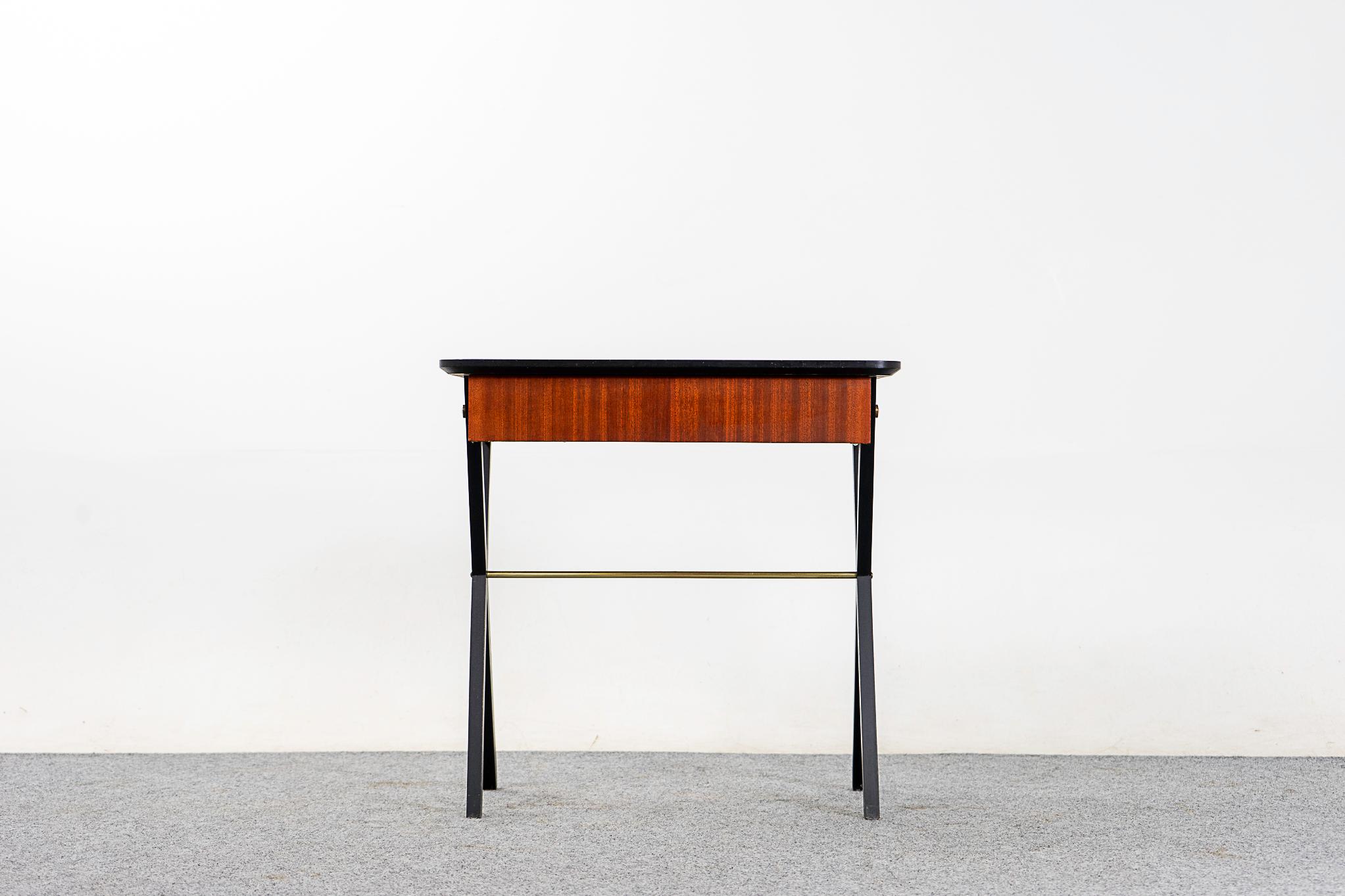 Mahogany midcentury side table, circa 1970s. Beautifully veneered case rests on slender, striking black contrasting X-crossed legs with polished metal support. Beautiful rounded edges and metal details, sleek drawer for your assorted sundries.