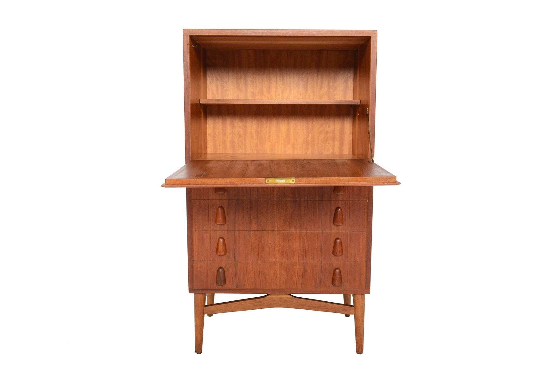 This Danish modern midcentury dry bar dresser in teak will be a wonderful addition to any modern home. This wonderful piece features a large drop down door which opens to expose a spacious interior with an adjustable shelf. Four drawers sit below