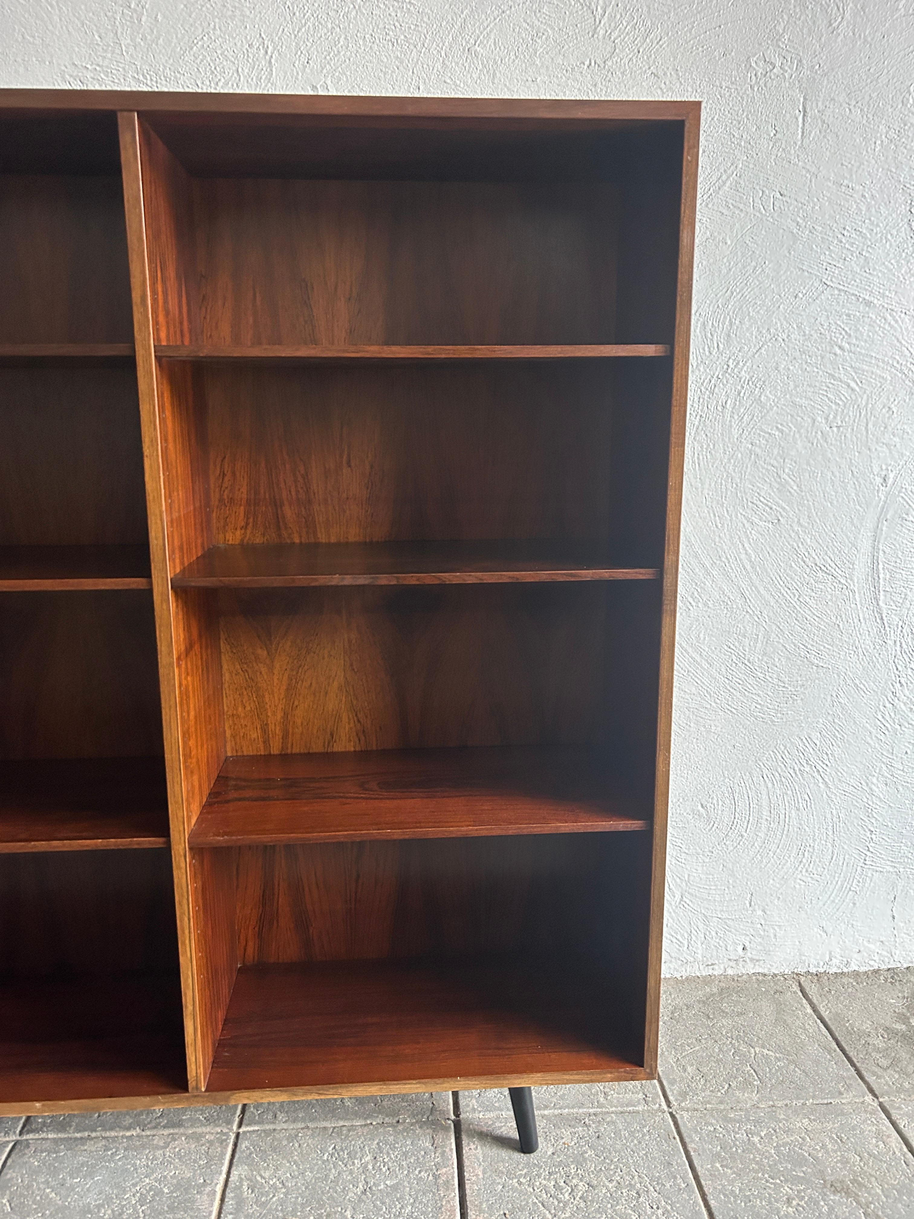 Beautiful simple Danish modern mid century rosewood wide wall floor bookcase. Has 6 adjustable shelves. Amazing rosewood grain! In great vintage condition, circa 1960. Labeled Gunni Omann - made in Denmark.

Measures 47” w x 11.5” d x 53” high