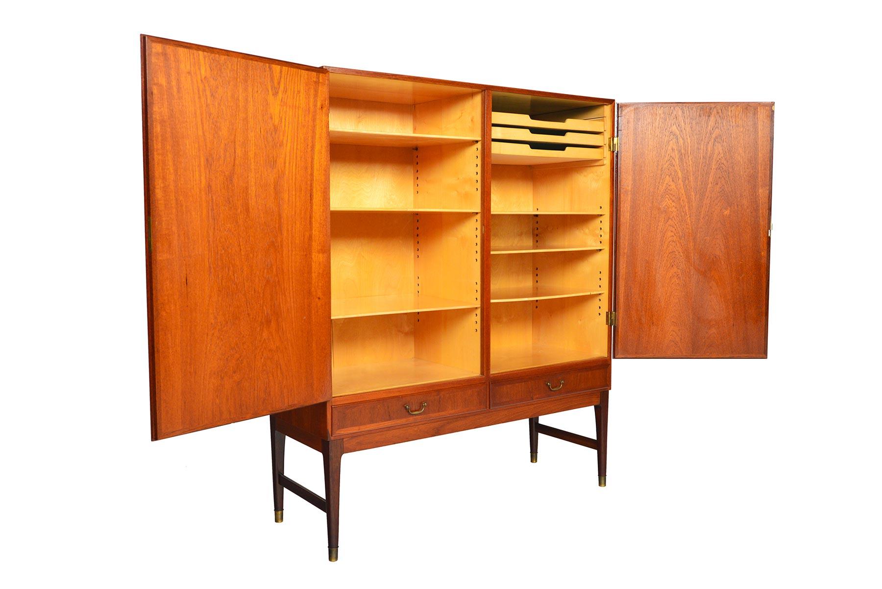 This Danish modern teak bureau offers a large storage capacity and sleek design. Two large locking doors open to reveal a beech- lined, two bay interior outfitted with six adjustable shelves and three drawers. Two lower drawers with original brass