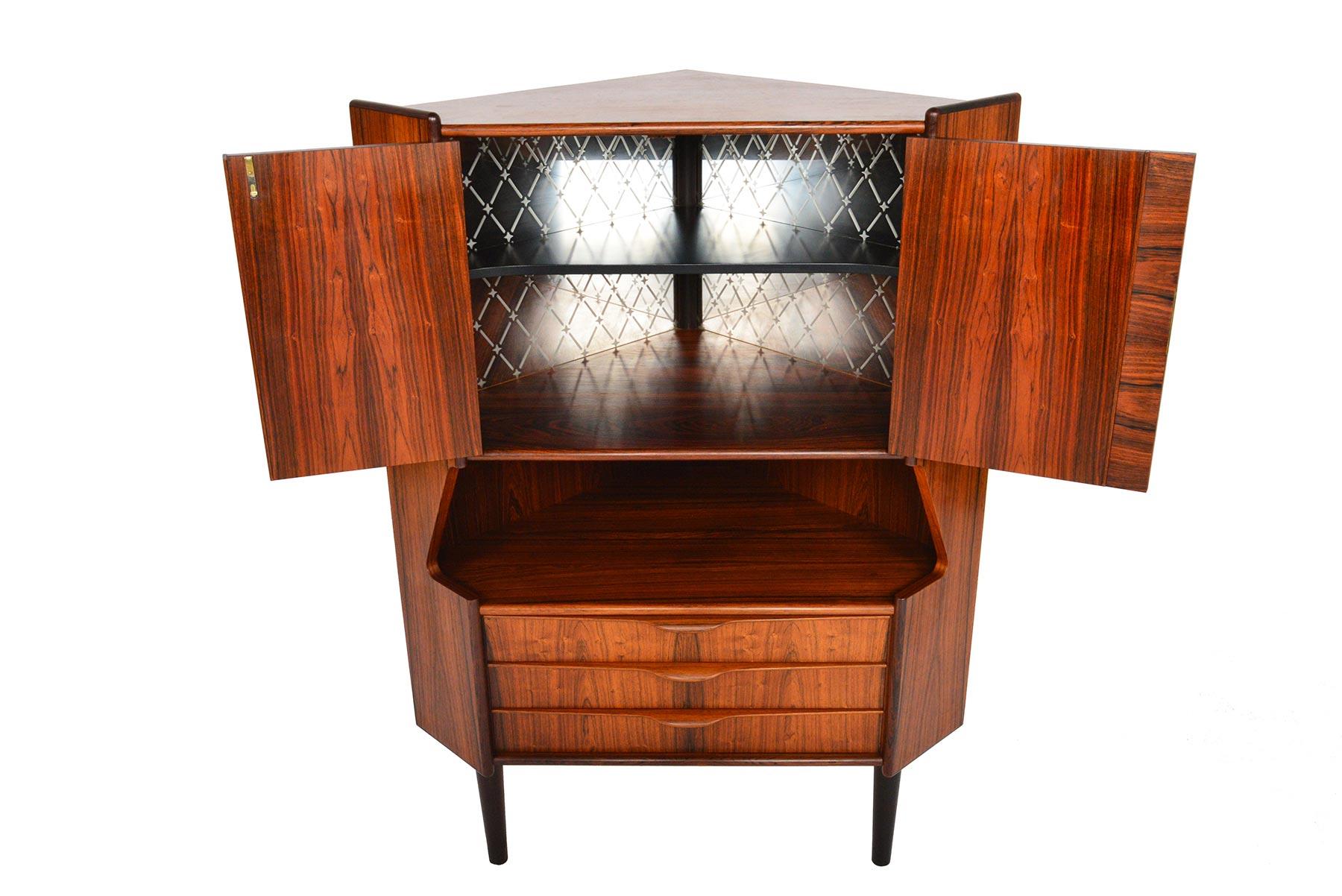 This fabulous Danish modern midcentury corner bar in Brazilian rosewood was designed by Gunni Omann for Omann Jun Møbelfabrik in the 1960s. This sharp piece features two locking cabinet doors which open to an etched, mirror backed bar cabinet