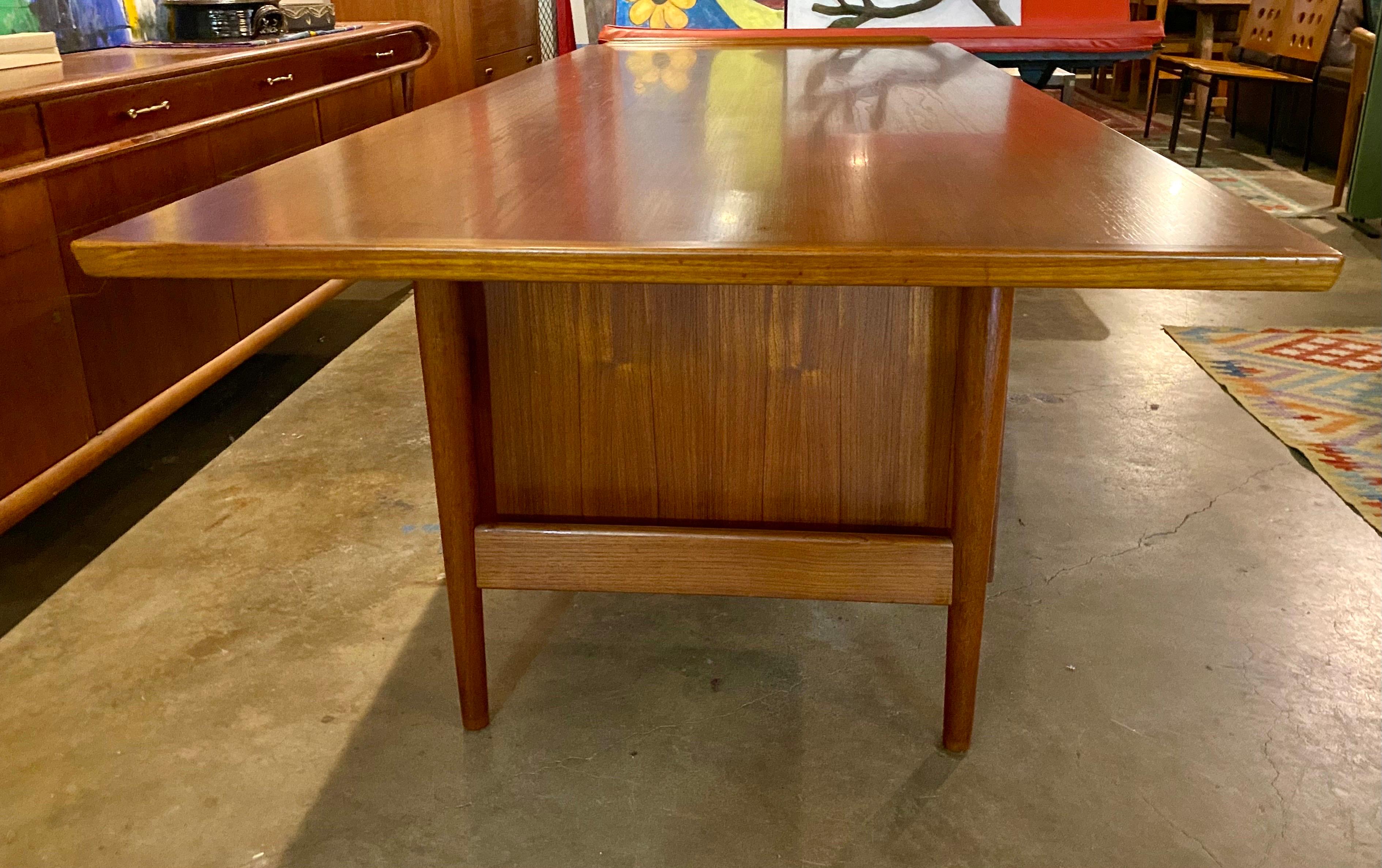 Large Danish modern 'Model 207' executive teak desk designed by Arne Vodder. This Danish mid-century modern features 3 drawers on the left and one drawer and a larger compartment on the right with teak pulls and has raised edges on both sides of the