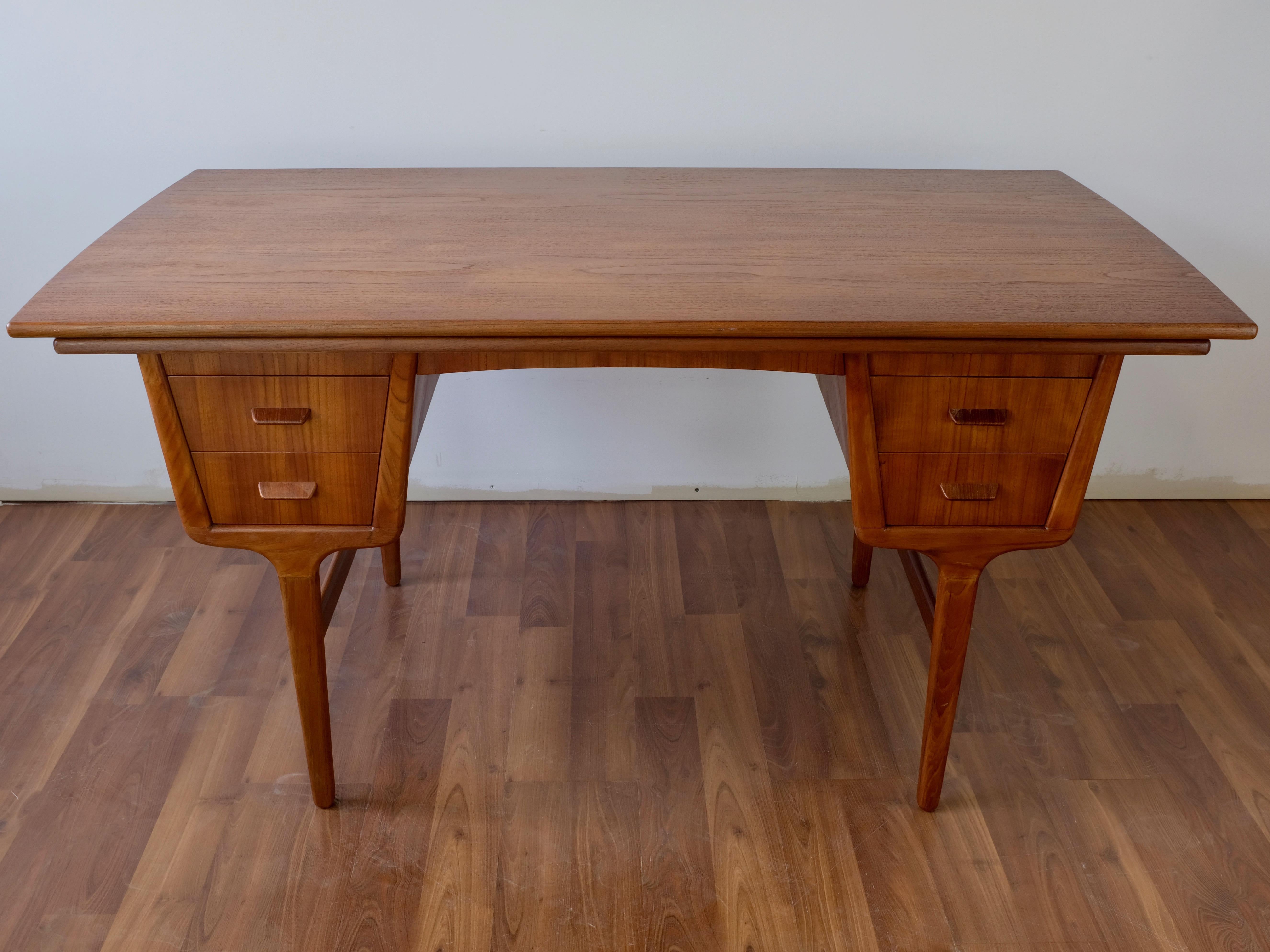 Double sided teak desk designed by Carl Aage Skov and made in Denmark by Munch Mobelfabrik

The piece has two banks of two drawers on one side, and one tall drawer and open compartment with shelf on the other side. The piece features draw leaves