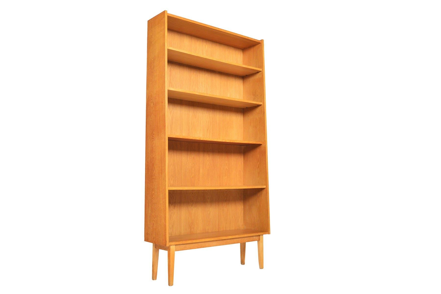 This stately Danish modern midcentury bookcase in oak is the perfect storage piece for any modern home. Three adjustable shelves provide versatility for storage. Case stands on a beautiful tapered oak base. In excellent original condition with
