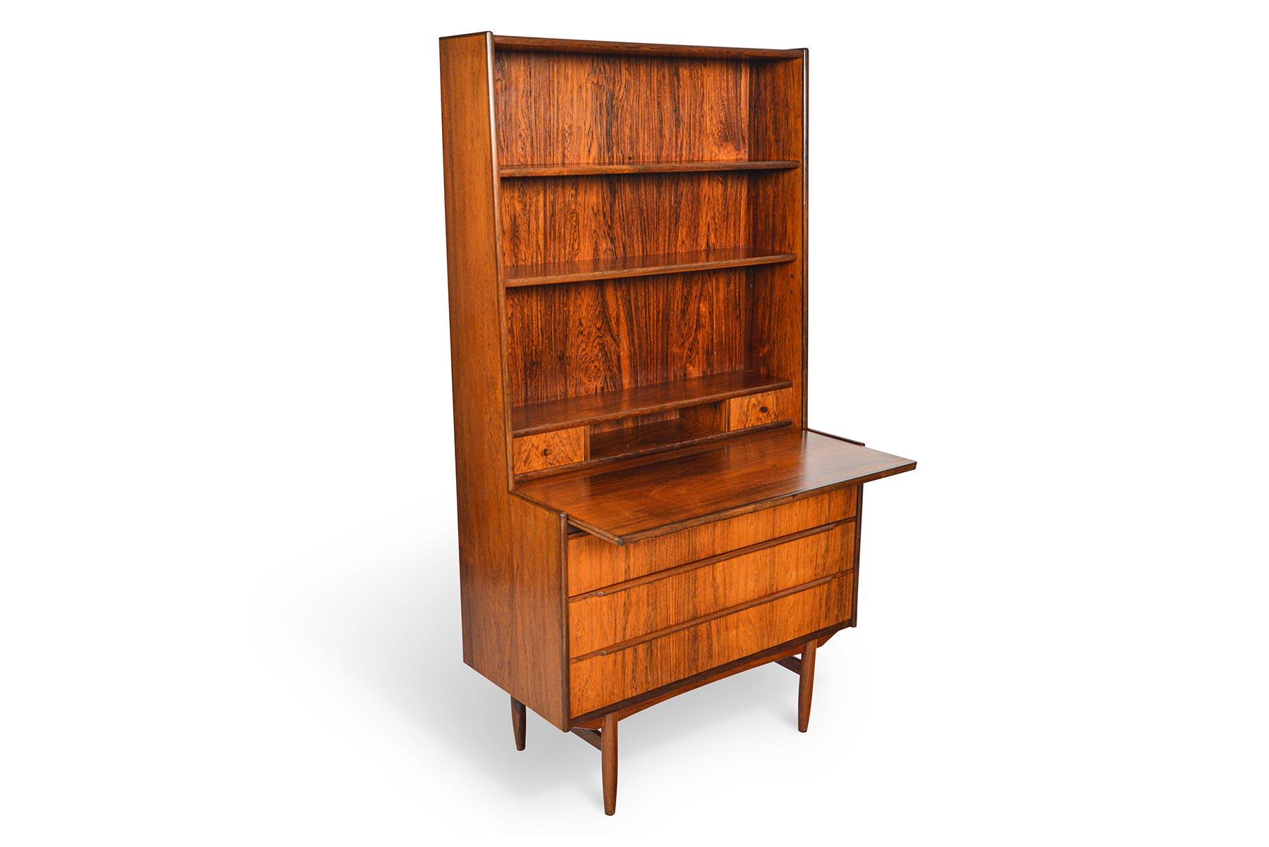 This beautiful Danish modern midcentury bookcase in rosewood offers a narrow footprint with vertical storage and a pullout desk! The tall bookcase back features one fixed and one adjustable shelf. The lower cabinet houses three large drawers. A