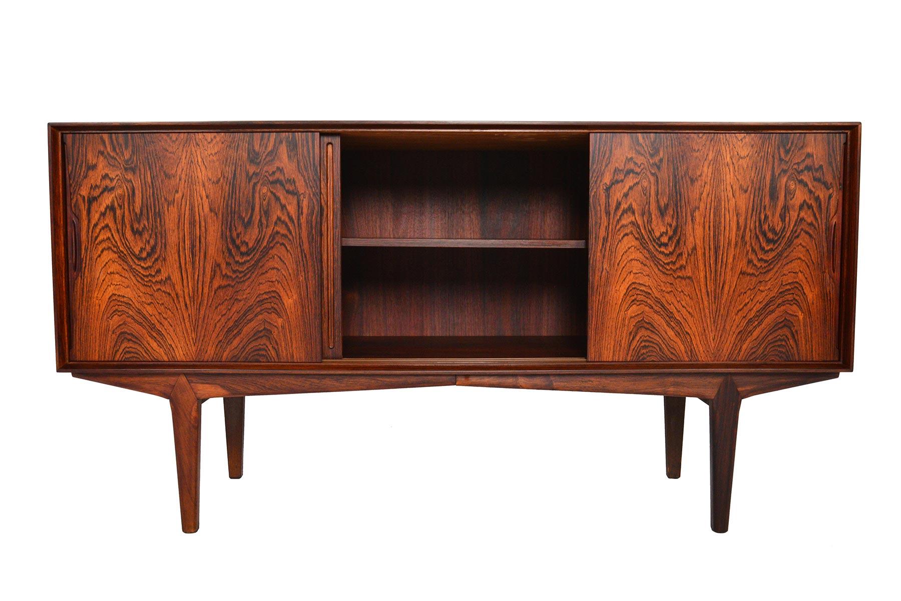 This gorgeous rosewood credenza model was designed by O. Frandsen for Knud Nielsen in the 1960s. Minimalist details and expert craftsmanship showcase dramatic book- matched Brazilian rosewood grain. Three sliding doors open to two bays outfitted