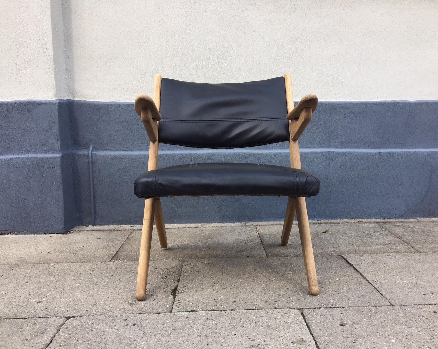 This sculptural lounge chair was designed by Arne Hovmand Olsen in Denmark during the early 1960s. It is made from solid oak and has been reupholstered in black leather. Due to the arched back, the leather is fitted rather loosely to the backrest.
