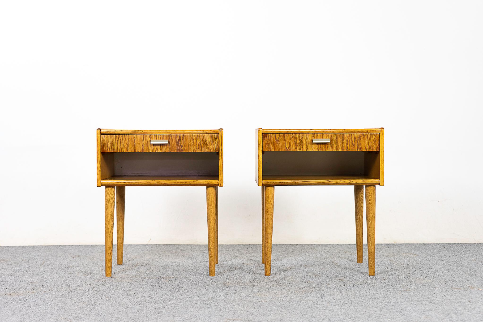 Oak bedside table pair, circa 1960's. Dovetailed drawer for small items, open cubby is perfect for your favorite book. Darling polished metal finger pulls, solid wood framing and matched veneer on top and sides. Front has small veneer repair. A