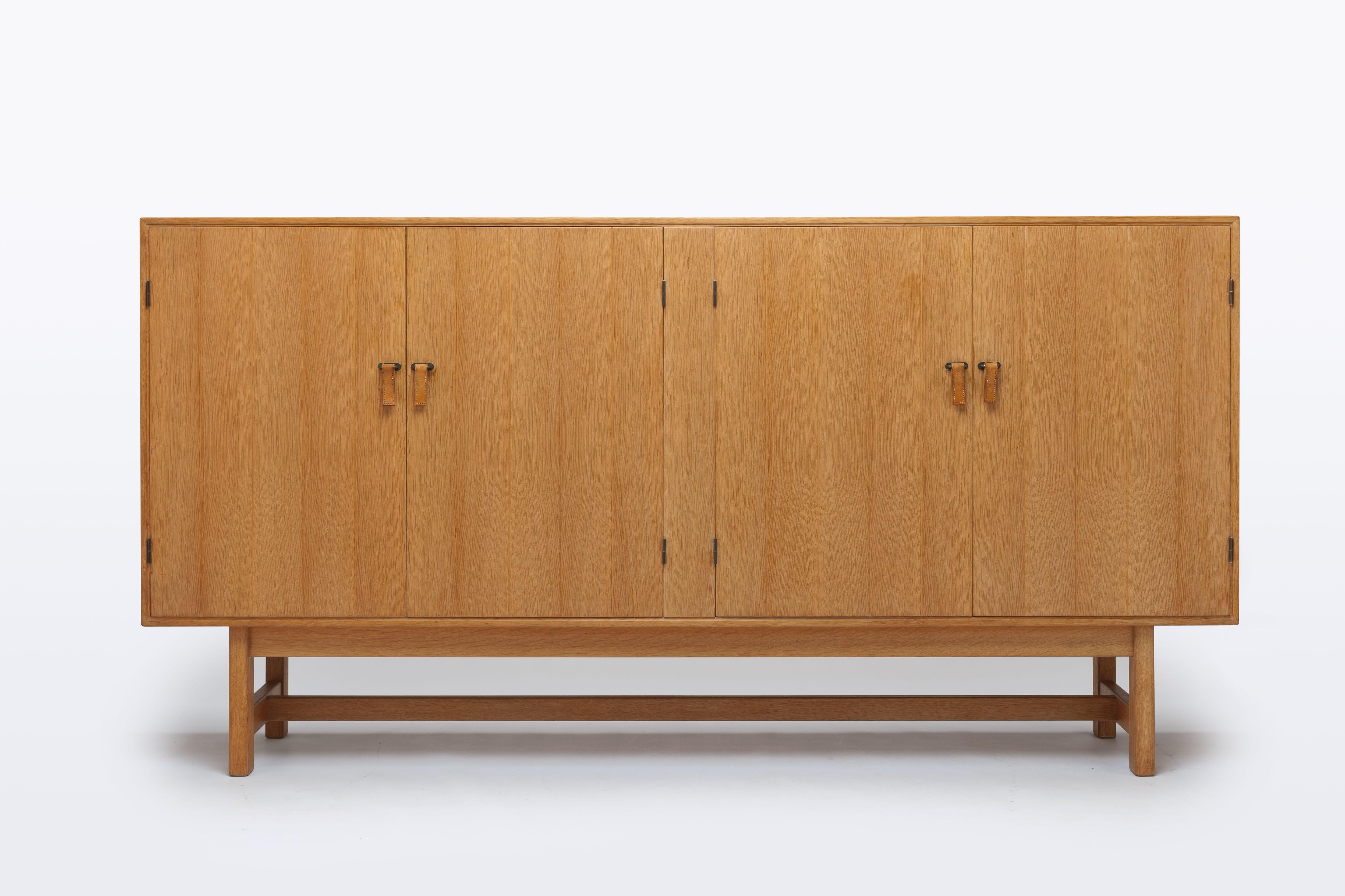 Beautiful minimalistic modern cabinet by Danish designer Kurt Kurt Østervig with paneled doors executed with leather pulls on brass hardware.
The cabinet is divided into four compartments, of which one is executed with typical Danish smaller trays
