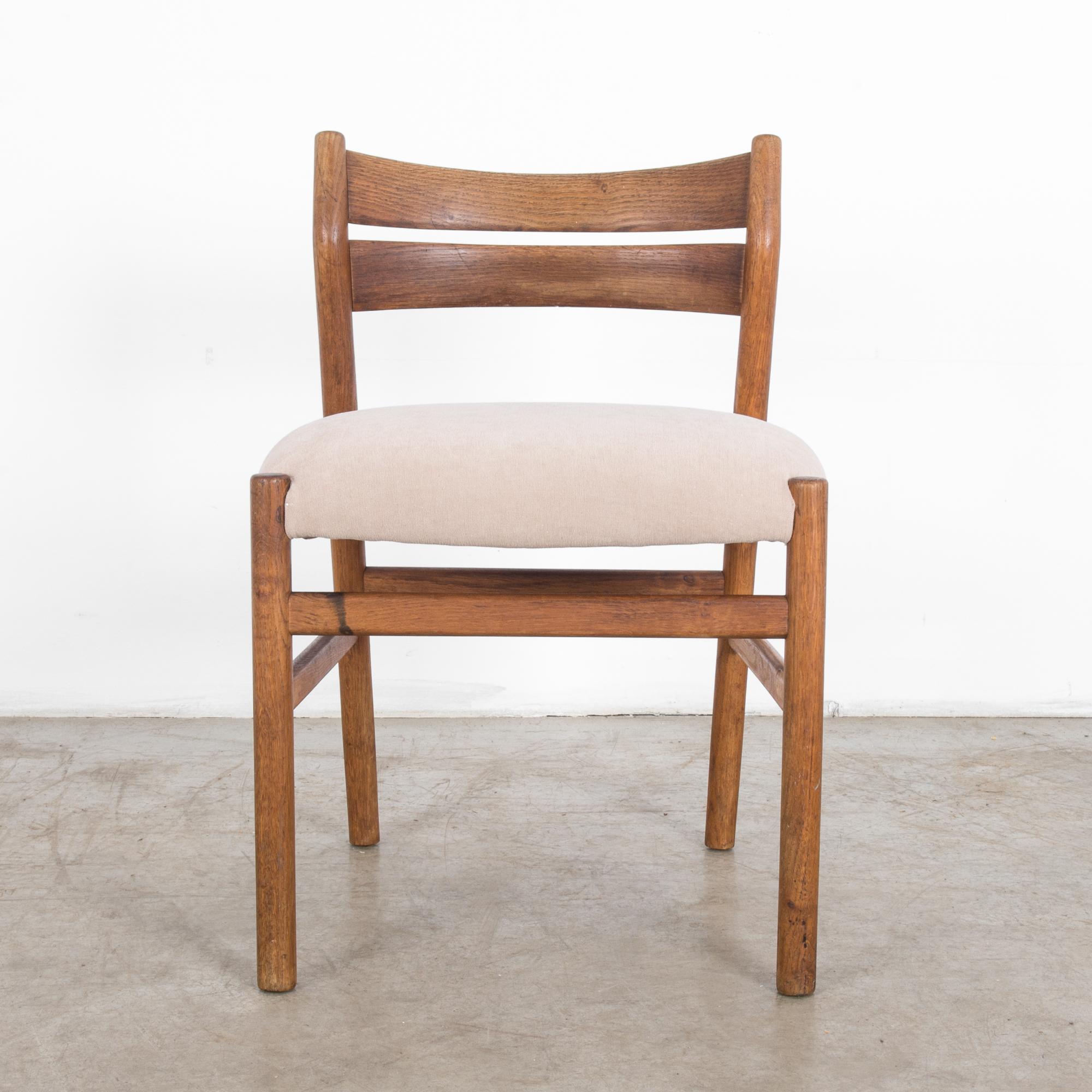 This oak chair was made in Denmark, circa 1960. The upholstered fawn seat rests on a wide and sturdy frame with stretchers on all sides. A pair of rails set on its low back curves gently, and the top tilts slightly backward. The warm, brown tone