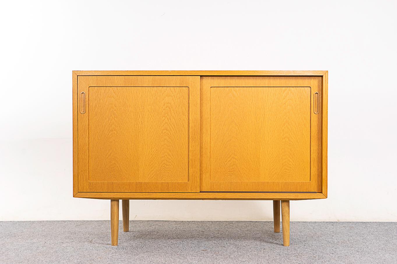 Oak Danish sideboard, circa 1960's. Smooth operating sliding doors, sleek tapered legs, 3 adjustable shelves and integrated finger pulls. Modern, simple lines. Hundevad & Danish Furniture Makers' control stamp intact.   

Unrestored item with option