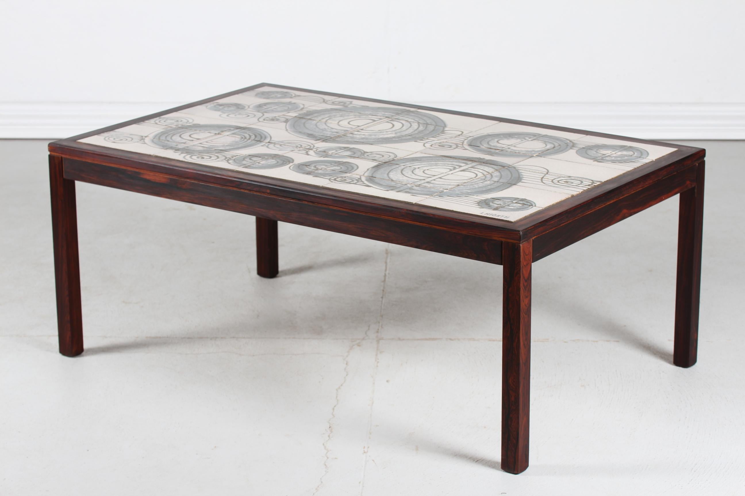 Danish Mid-century coffee table made from dark wood with inlaid ceramic tiles from the ceramic studio L. Hjorth. Made ca 1960s.
The tiles have a handpainted abstract decor in brown and blue on beige. 

One tile with signature: L Hjorth.



 