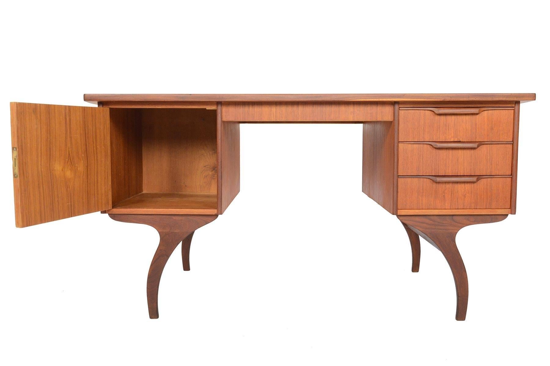 This Danish modern midcentury writing desk in teak is simple in concept but is brimming with organic design details. This unusual design offers a large locking cabinet and a bank of three drawers flanking the kneehole. Beautifully contoured