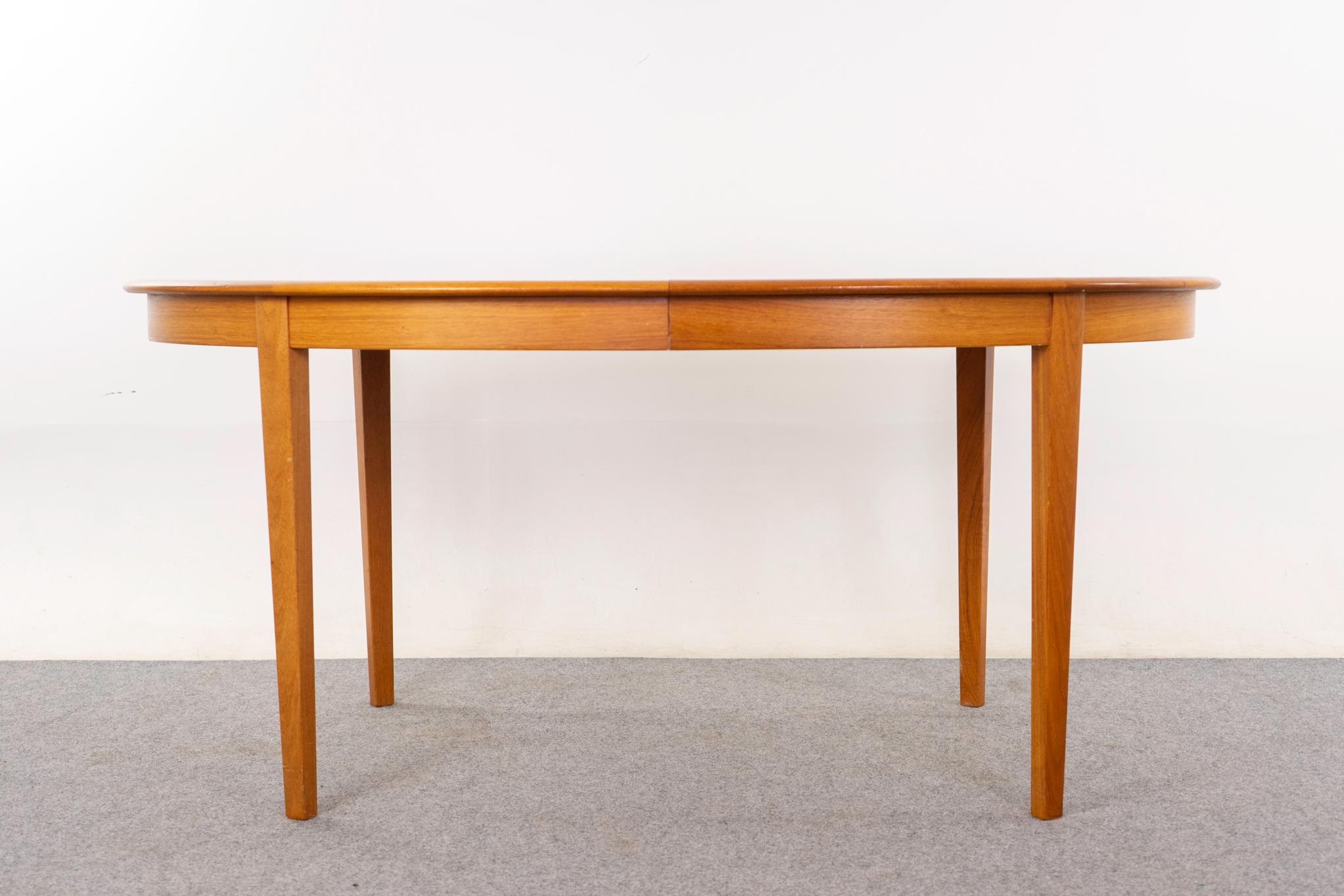 Teak Danish dining table, circa 1960's. Oval top is framed in solid scalloped teak edging, the center panels are golden veneer with book-matched grain. Add in the leaves to extend as needed. Leaves have optional skirting, for a continuous look when