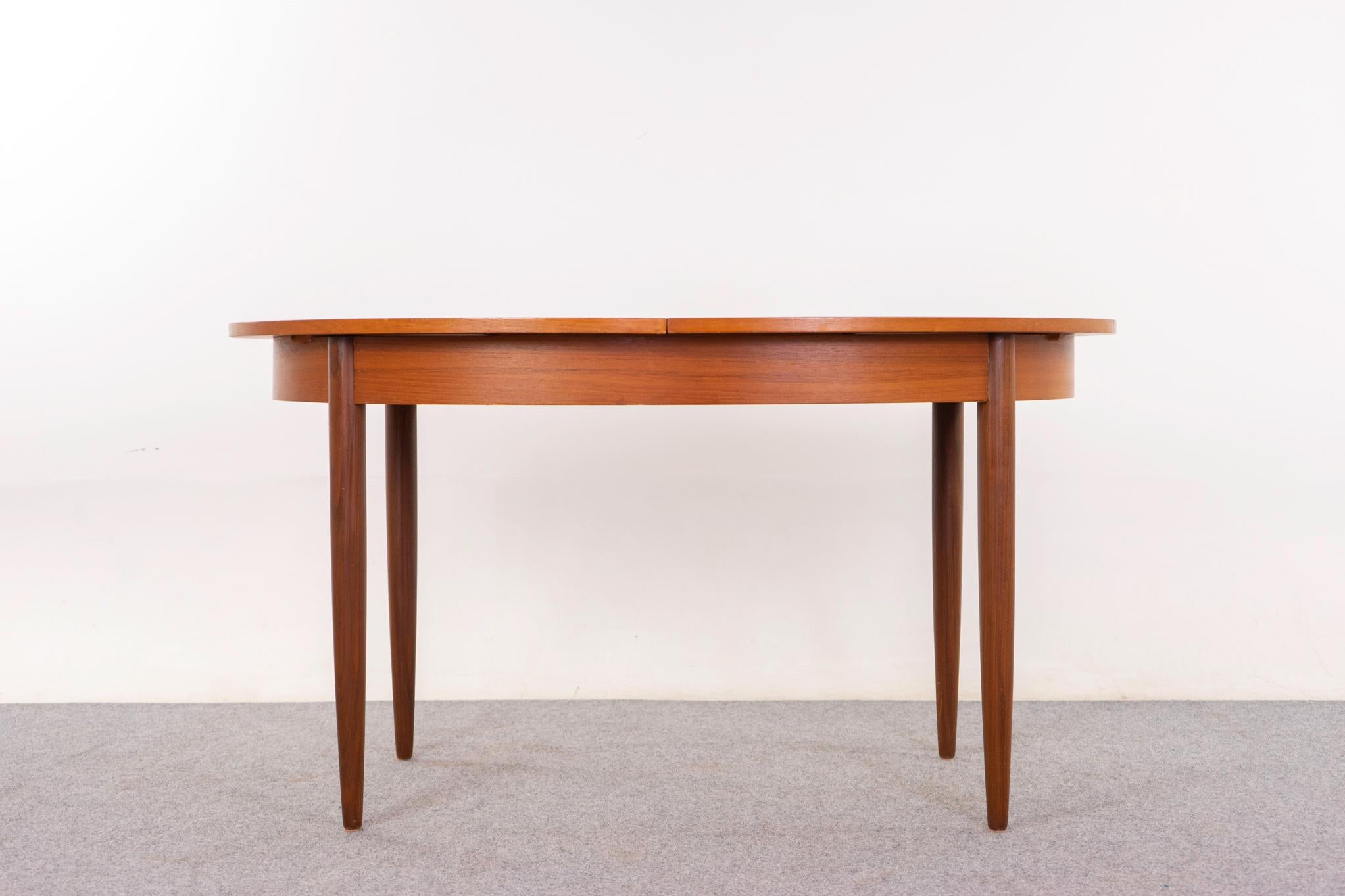 Teak Danish dining table, circa 1960s. Oval top is framed in solid wood trim, the center panels are golden veneer with book-matched grain. Self storing butterfly leaf is easily accessible, extend as needed! Contrasting tapered legs. Great as is