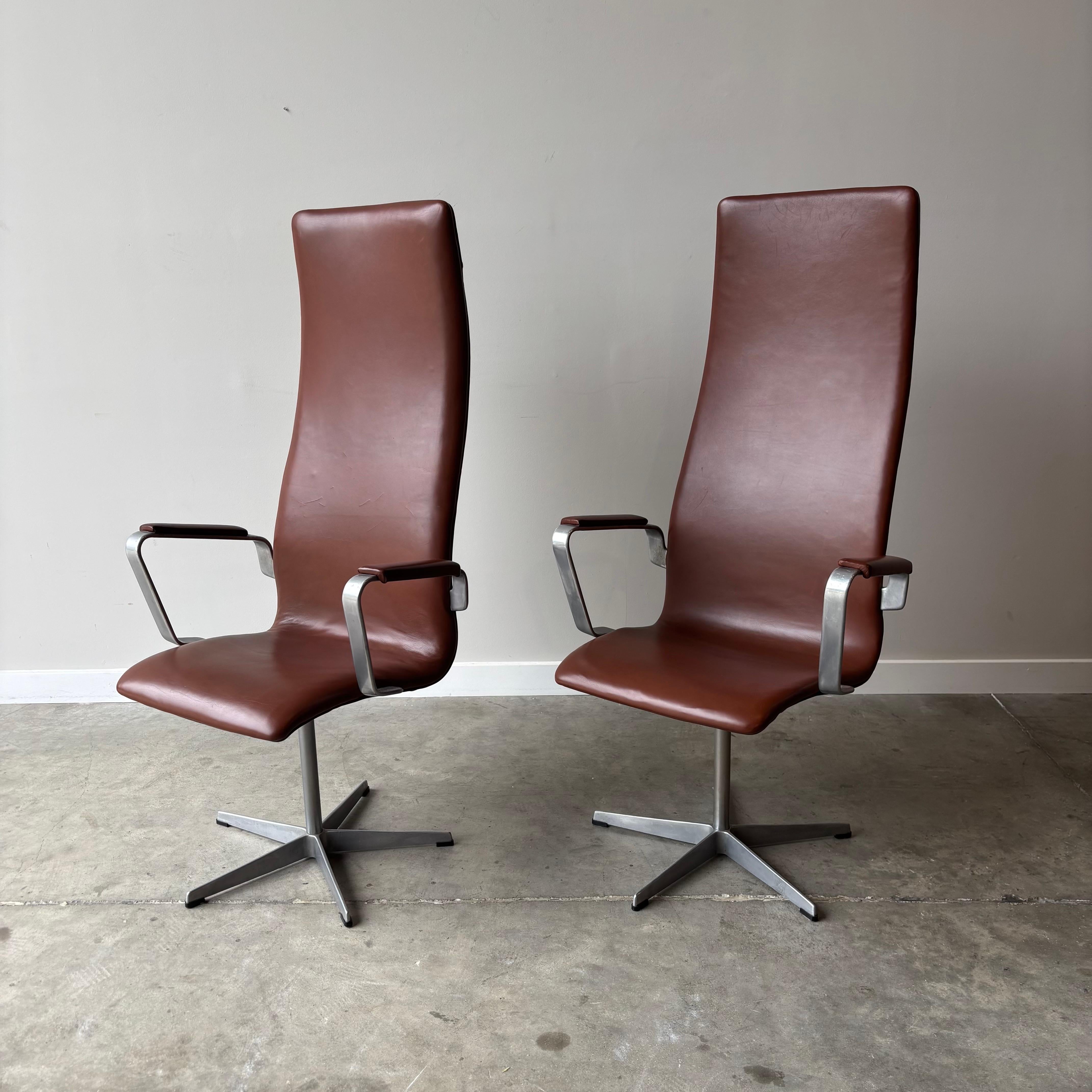 A stunning pair of Oxford dining chairs, created by Danish designer Arne Jacobsen for Fritz Hansen. The chairs showcase Jacobsen's signature mid-century aesthetic with their elevated backrest design and distinctive five-point metal base. Known for