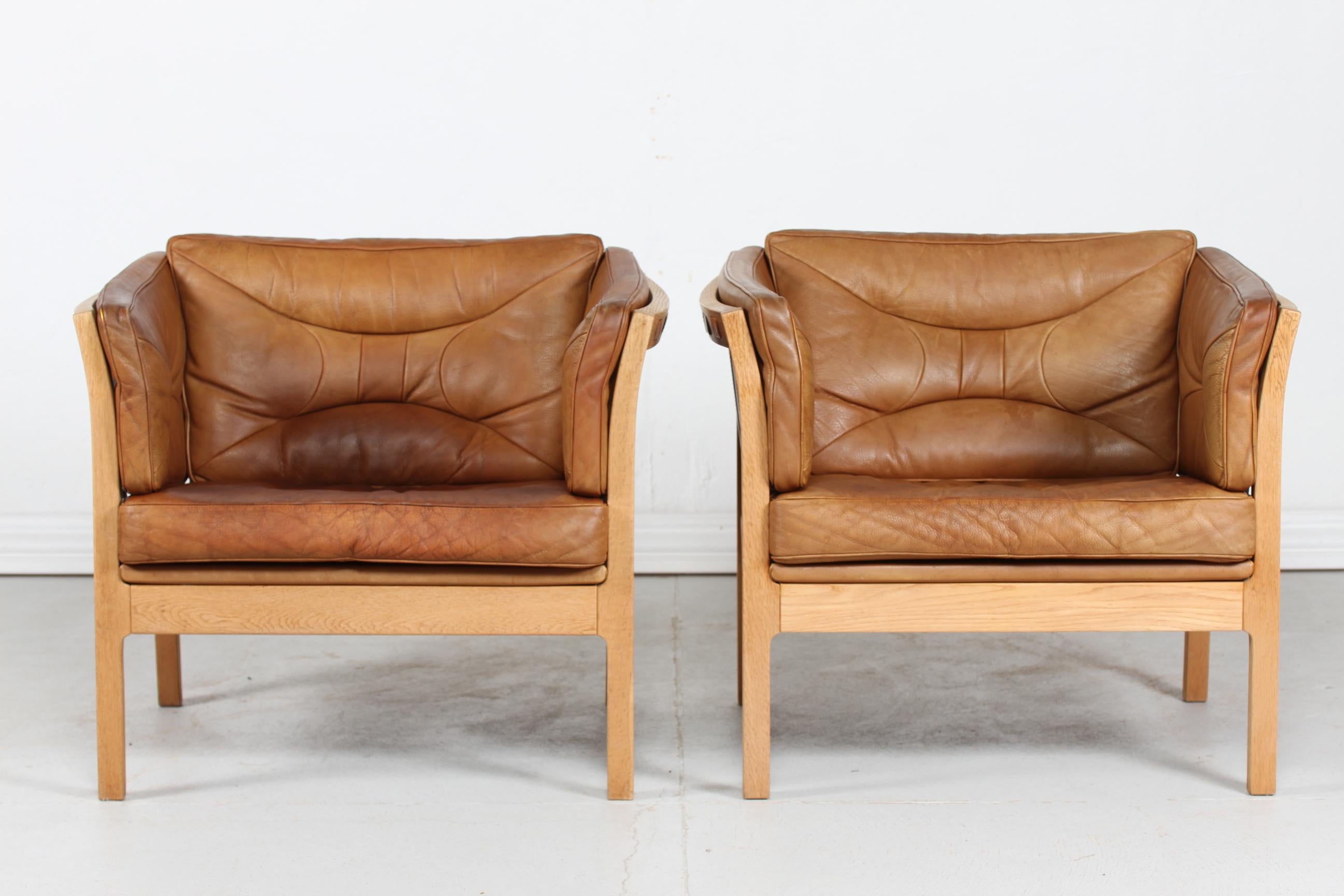 Danish modern pair of easy chairs or lounge chairs. 
They a made of oak with strips and cushions of genuine leather.

The chairs remain in very nice vintage condition with good patina - see photos.