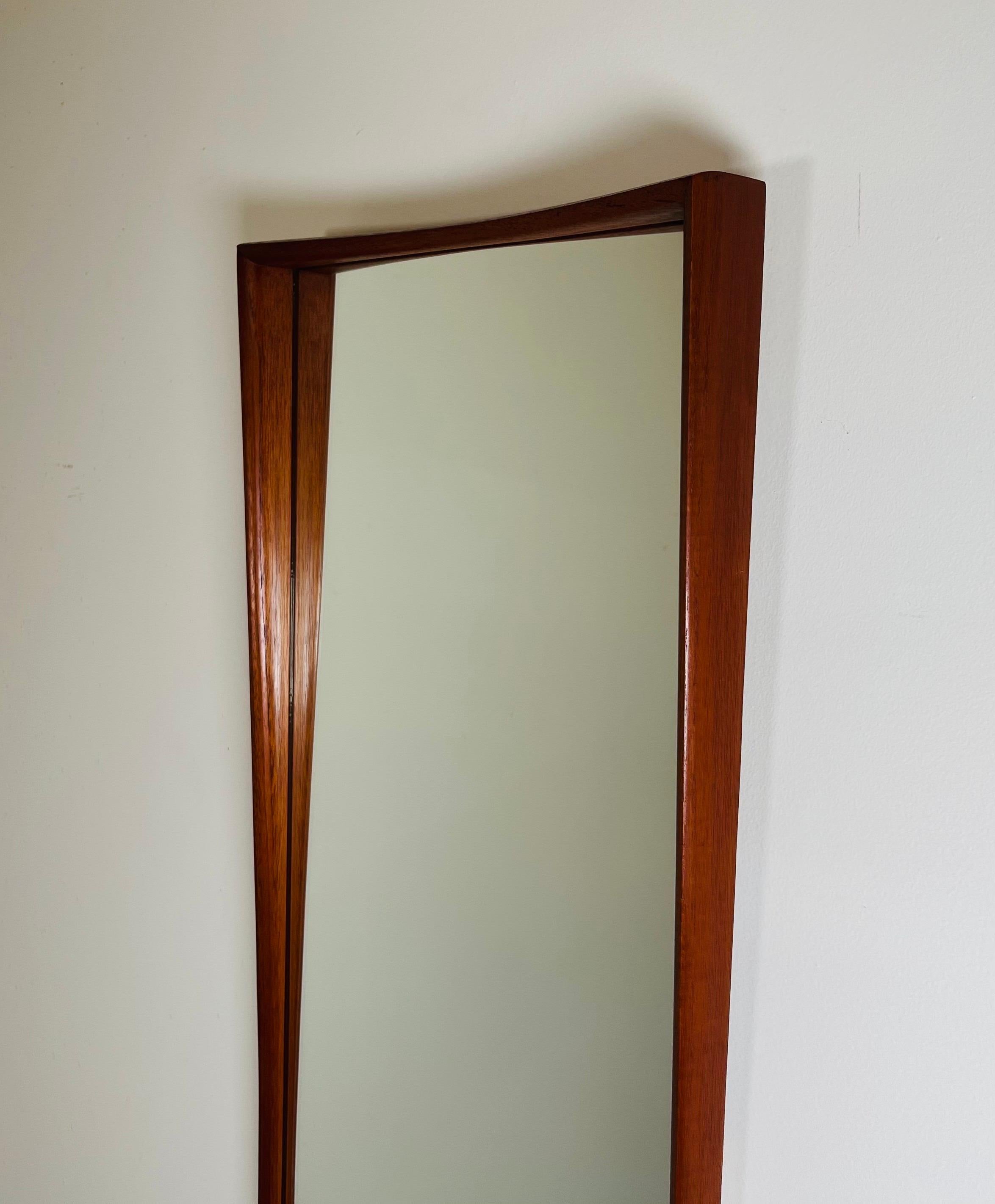 An elegant teak wall mirror by Asbjorn-Mobler having a curved teak sculptural frame that brings the wall upon which it is hanged to life. This lofted design is a cut above the average flat framed mirror. A touch of careful design that enhances its