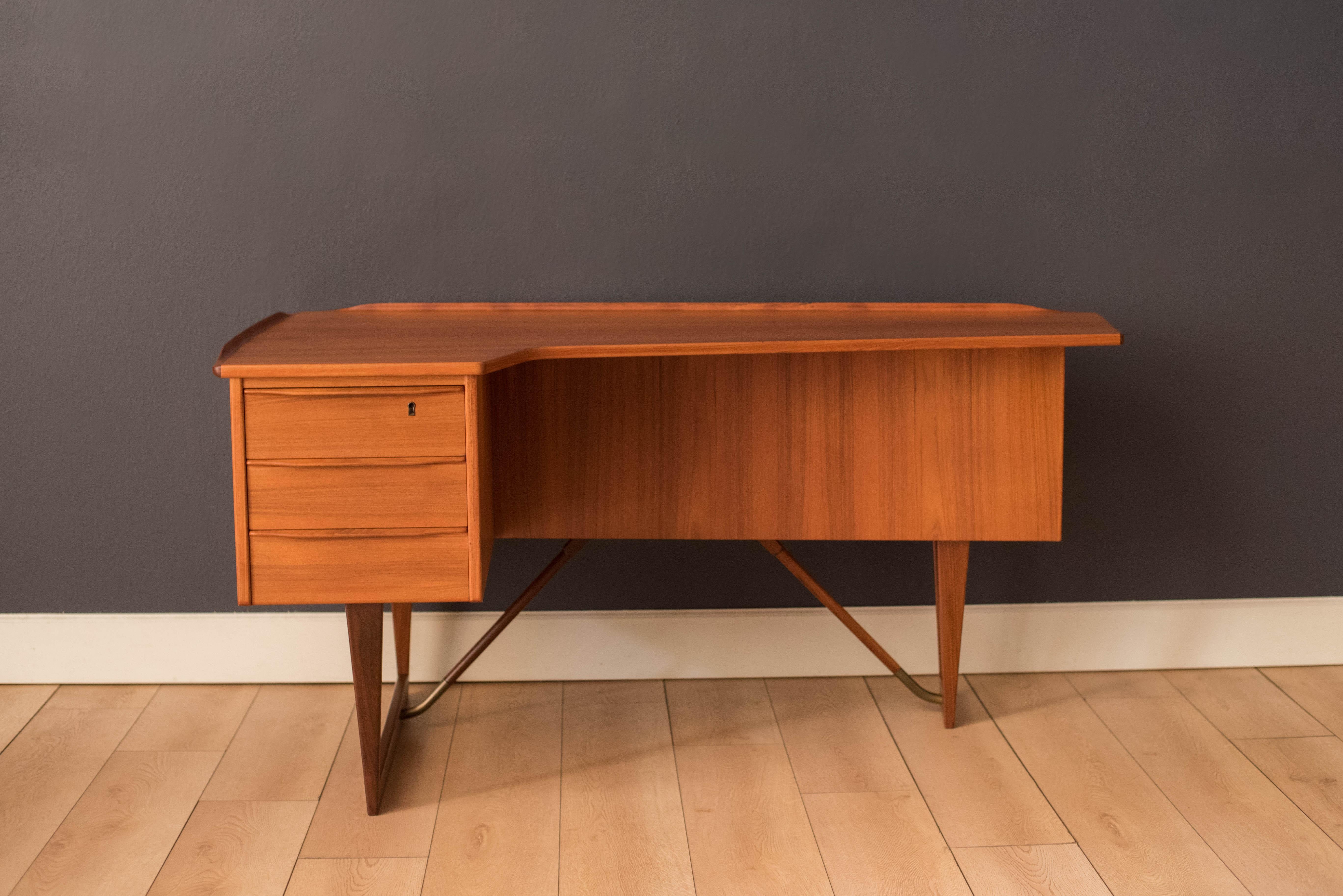 Mid-Century Modern writing desk in teak designed by Peter Lovig Nielsen for Dansk circa 1960's. Features a unique boomerang shaped top with a raised lip edge and tapered legs with brass supports. This piece includes three dovetailed drawers accented