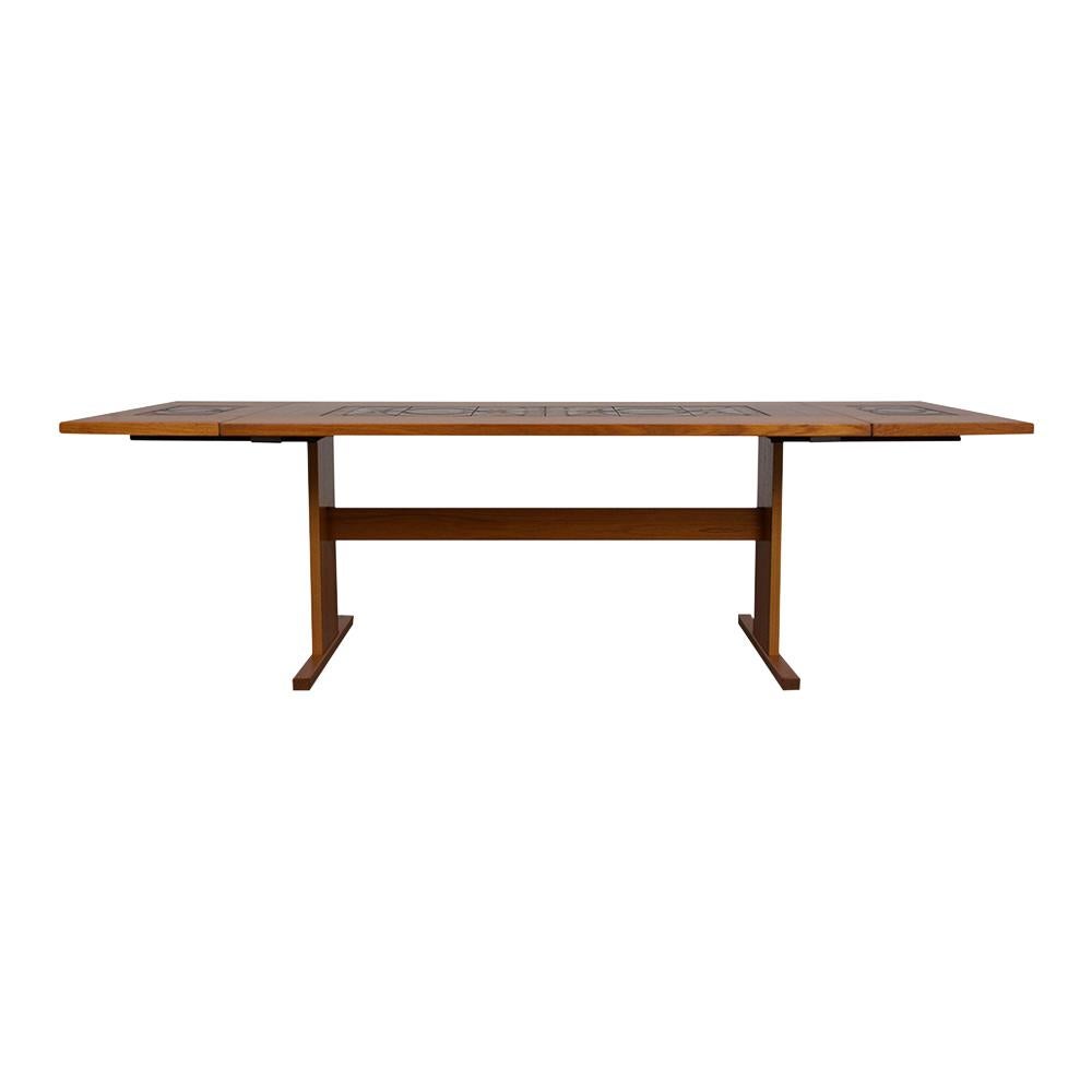 This Modern Danish Dining Room Table by Poulsen is made from teak wood and has its original walnut color with a patina finish. This extendable table features two drop leaves, ceramic inserts on the tabletop and the leaves sit on an unusual trestle