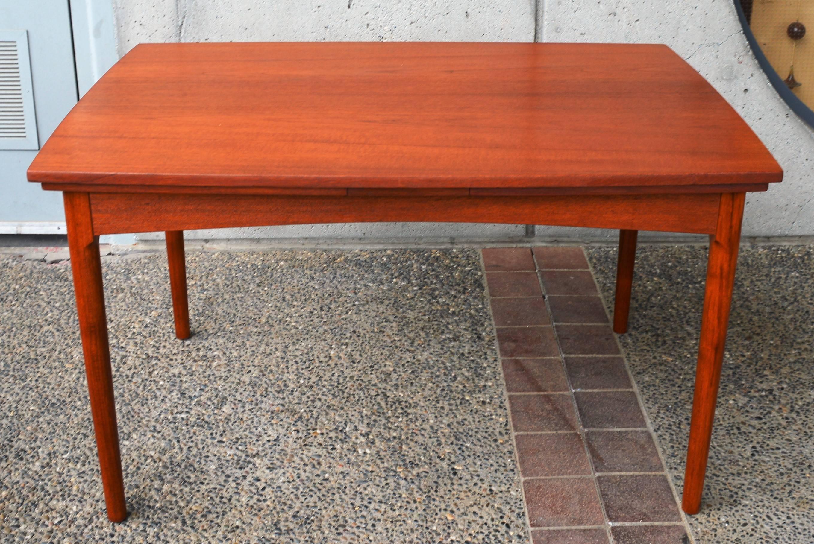 This gorgeous and rare Danish Modern teak quality dining table is an early one by Hundevad & Co. and features all wood construction, a surfboard shape (flares at the center and tapers towards the ends) and two leaves that stow under the table top
