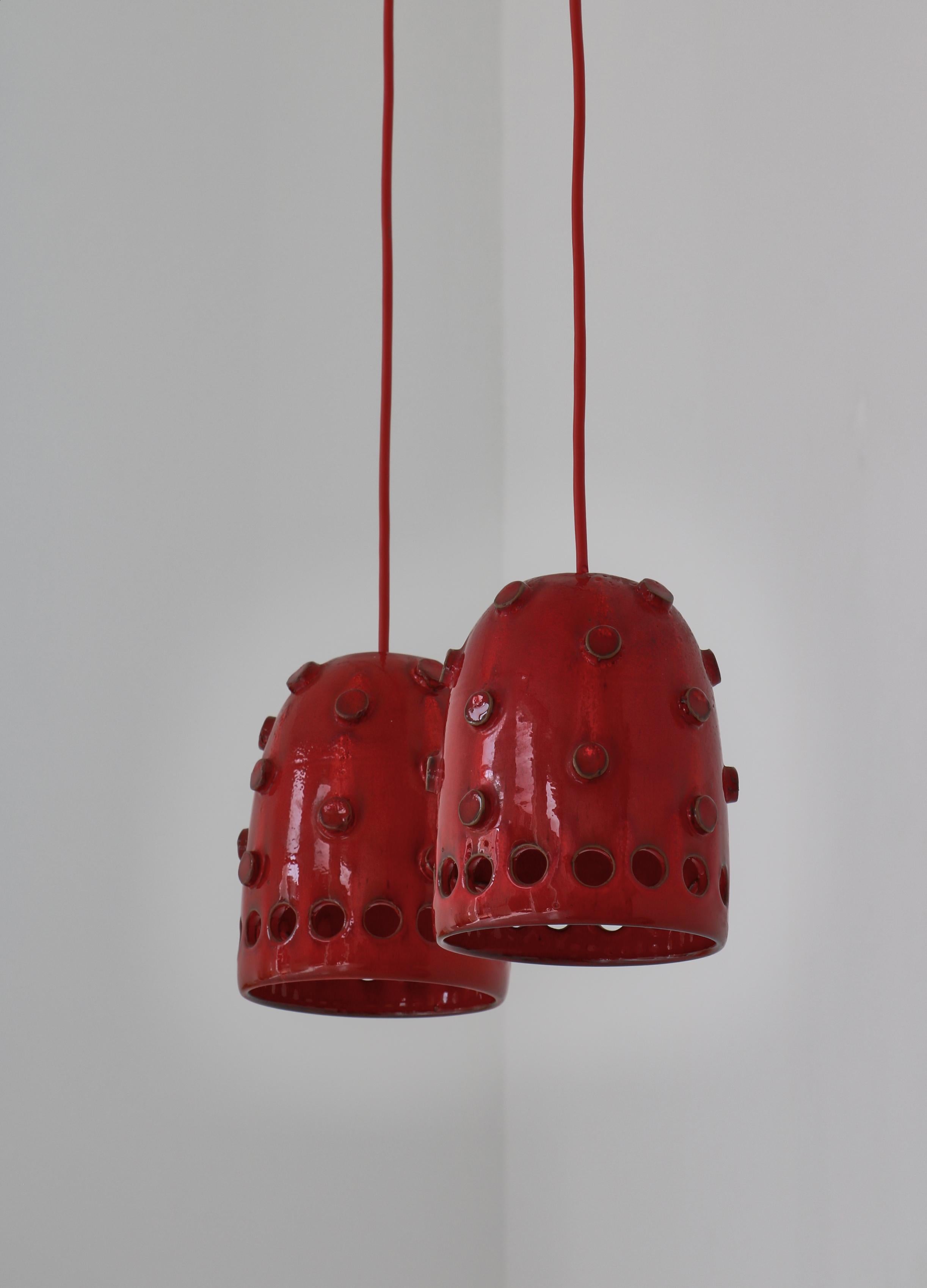 Unique Danish Modern pendants handmade in the 1970s by artist Jette Hellerøe at Axella studio, Denmark. The lamps are made from stoneware and finished in an expressive glossy red glazing. Original red wire included.

While Hans J. Wegner, Kaare
