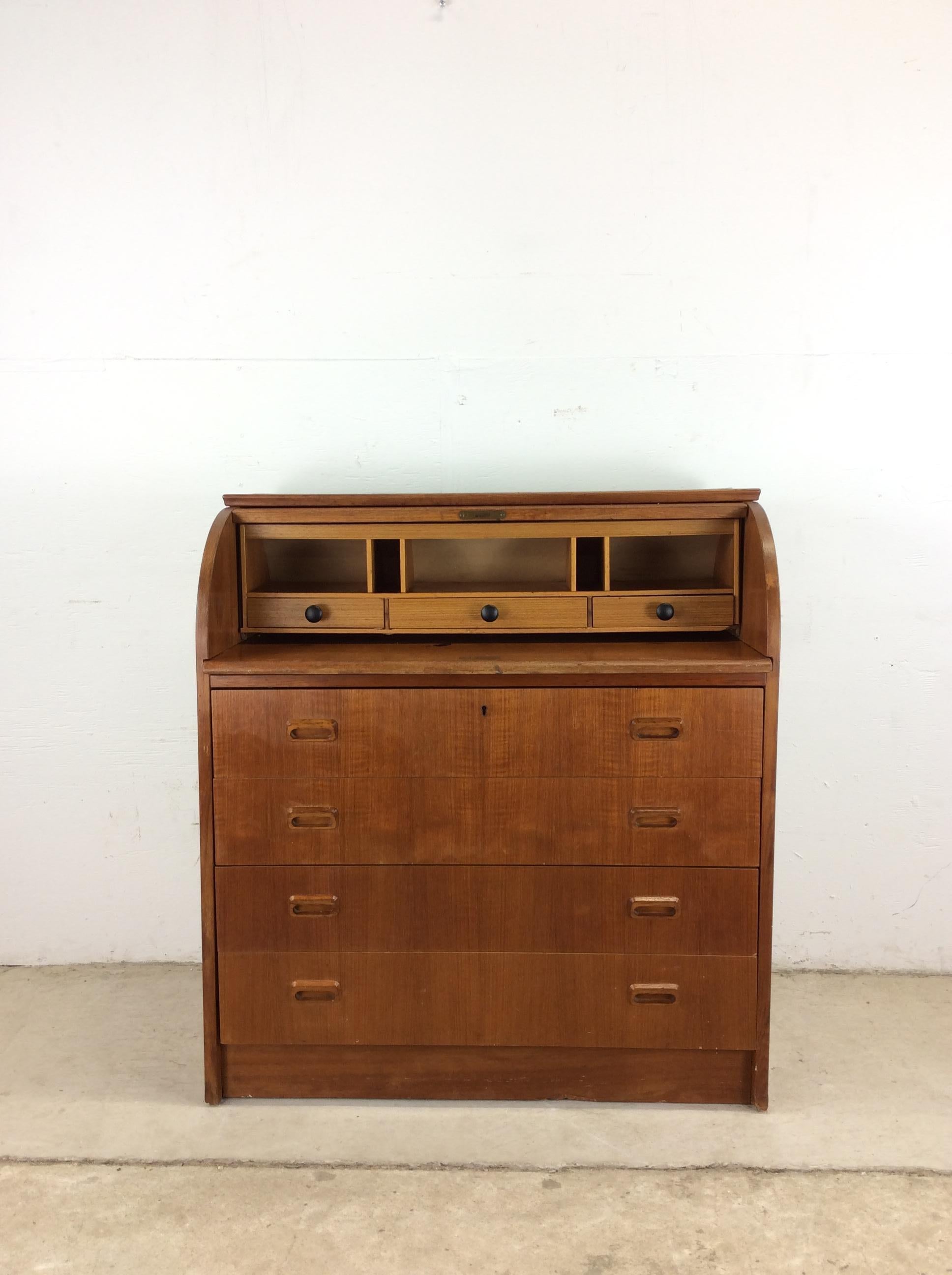 This Danish Modern rolltop desk features pressed wood construction, teak veneer with original finish, three small drawers up top, open storage above, draw leaf writing surface, four dovetailed large drawers with carved pulls.  Pulls out to 27