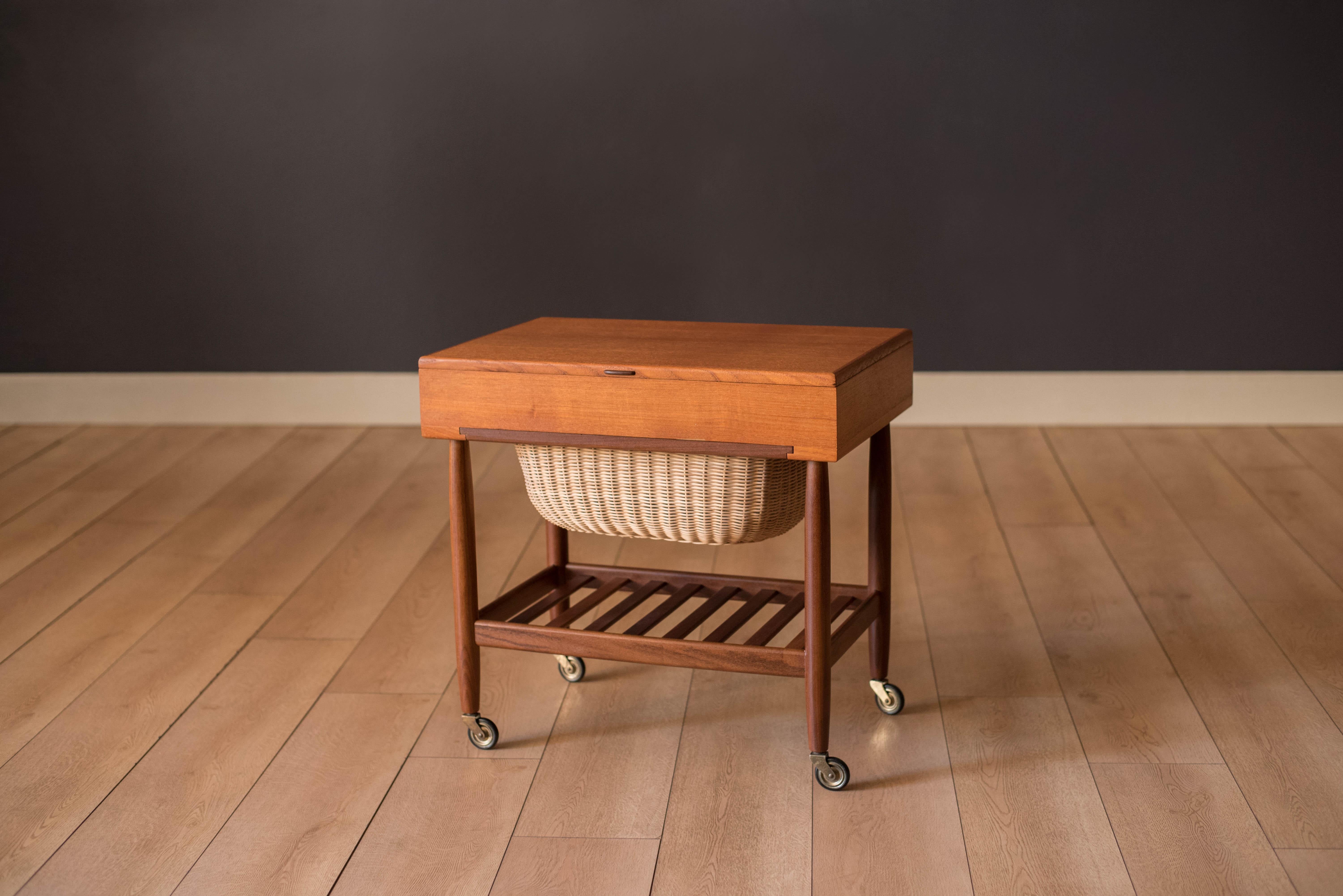 Mid century modern sewing end table in teak designed by Ejvind A. Johansson for FDB Mobler, Denmark. This two-tone piece is made with old growth teak featuring a storage organizing compartment with dividers, a seamless slide-out wicker basket tray,