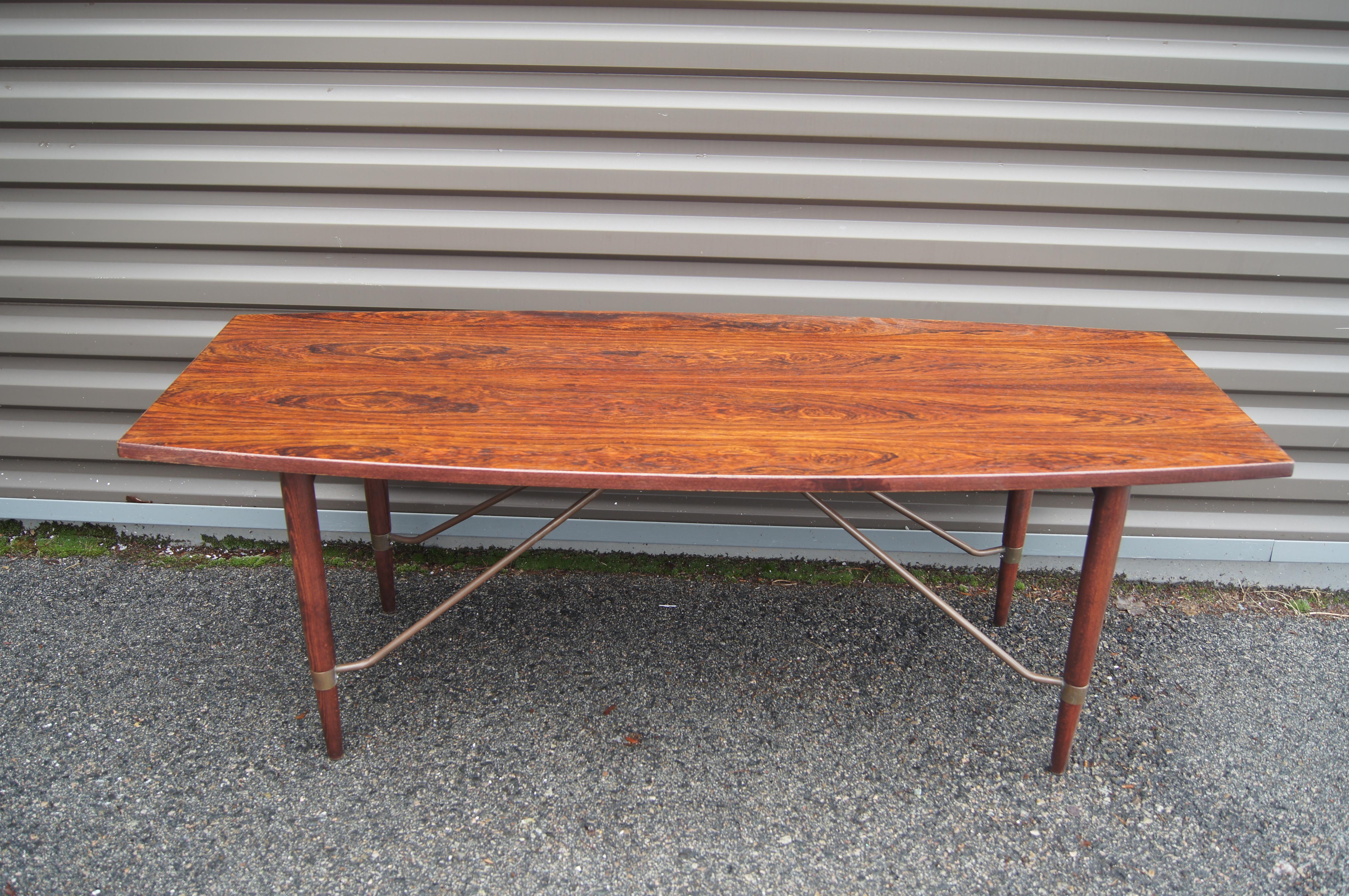 The tapered legs of this unusual Danish Modern rosewood coffee table are braced by copper supports extending from below the gently curved top. The grain of the rosewood surface is striking.