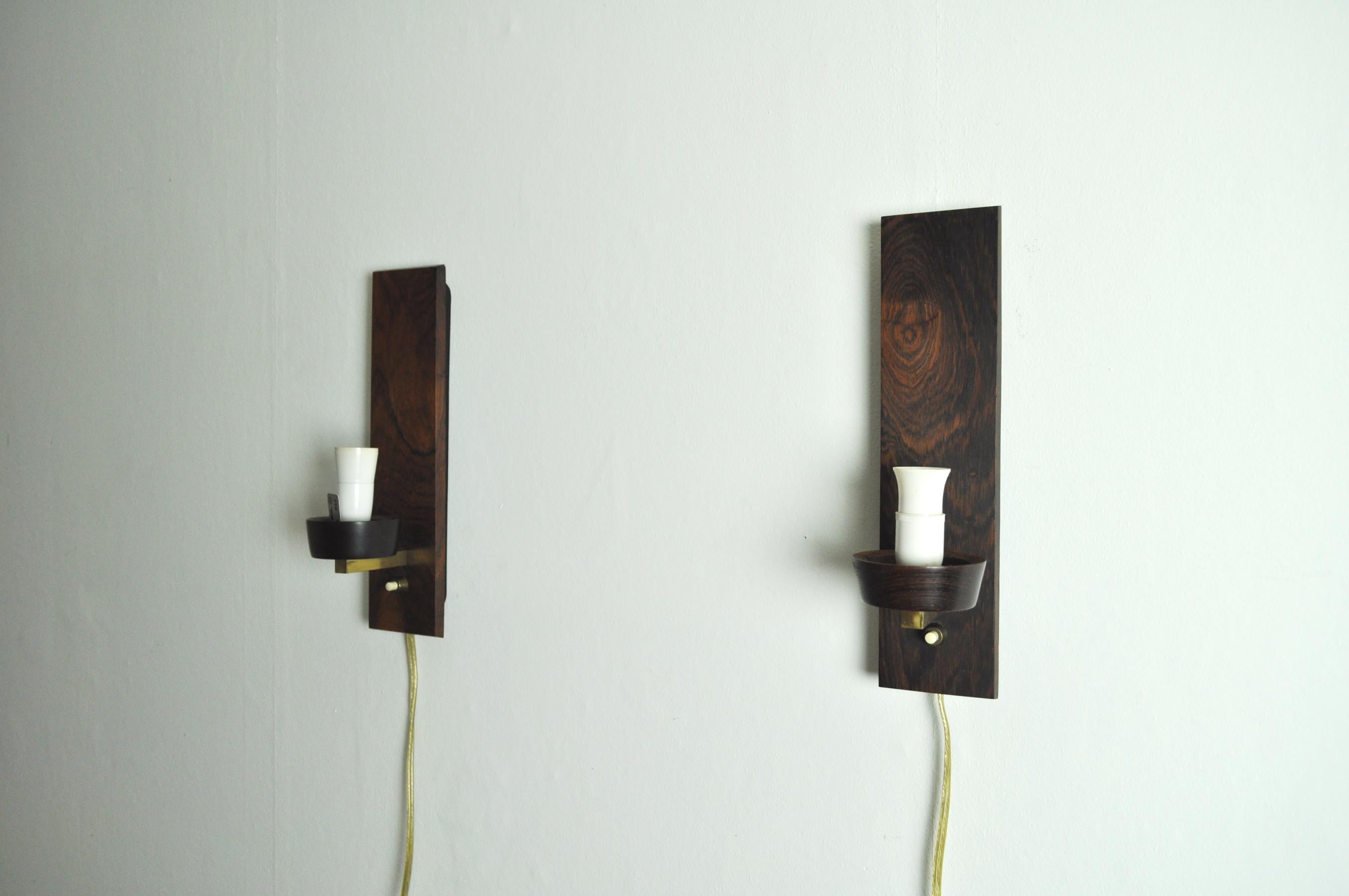 A pair of Danish modern rosewood and glass wall sconce by Lyfa in the 1960s.
The design features a back in black metal and rosewood, Fine brass details and rosewood holder for the white and transparent glass shade.
Excellent vintage