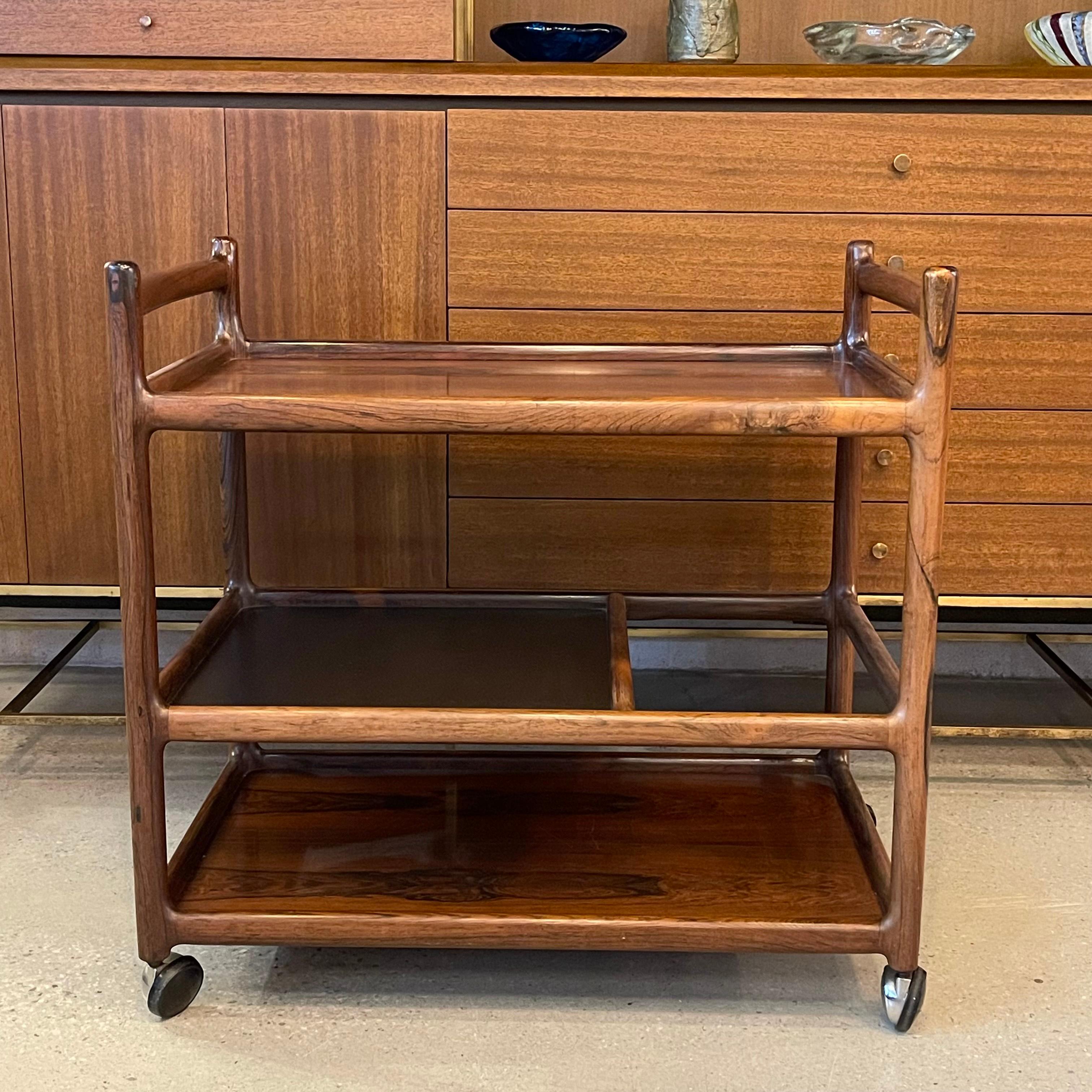 Elegant, Danish modern, rosewood bar, serving cart by Johannes Andersen for CFC Silkeborg features 3 tiers to accommodate glasses and bottles. The middle tier has a black laminate top that is wipeable. The chrome casters and handles make it easy to