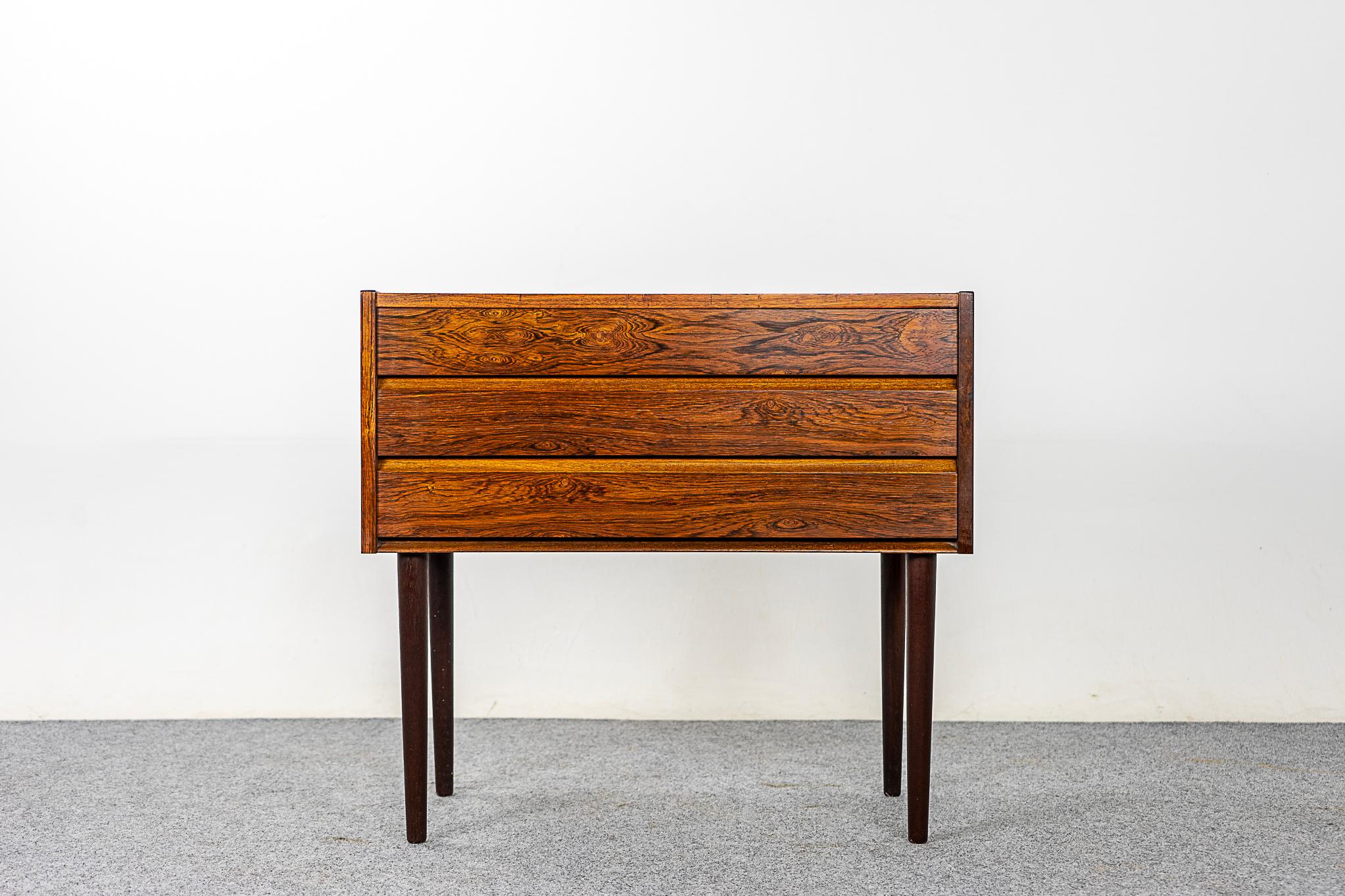 Rosewood Danish bedside/entryway dresser, circa 1960's. Beautifully veneered case with integrated sleek handles. Three dovetailed drawers, storage for small items. Slender, tapered, solid wood removable legs.