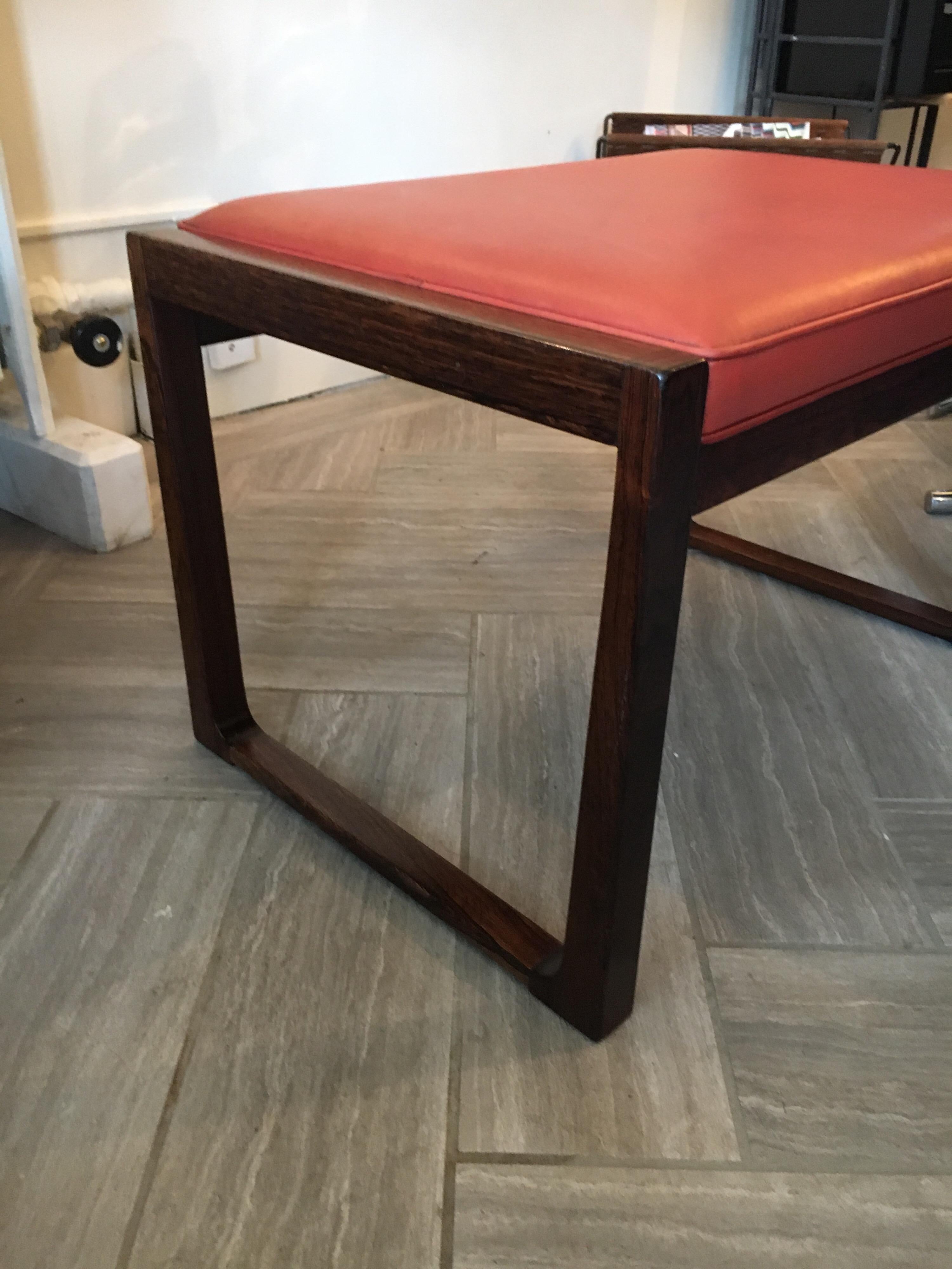 Chic little Danish modern rosewood bench with original rust red leather, circa 1960s. Can be used as a footstool, an extra seat, or as a coffee table or ottoman to add a touch of Mid Century Modern style.