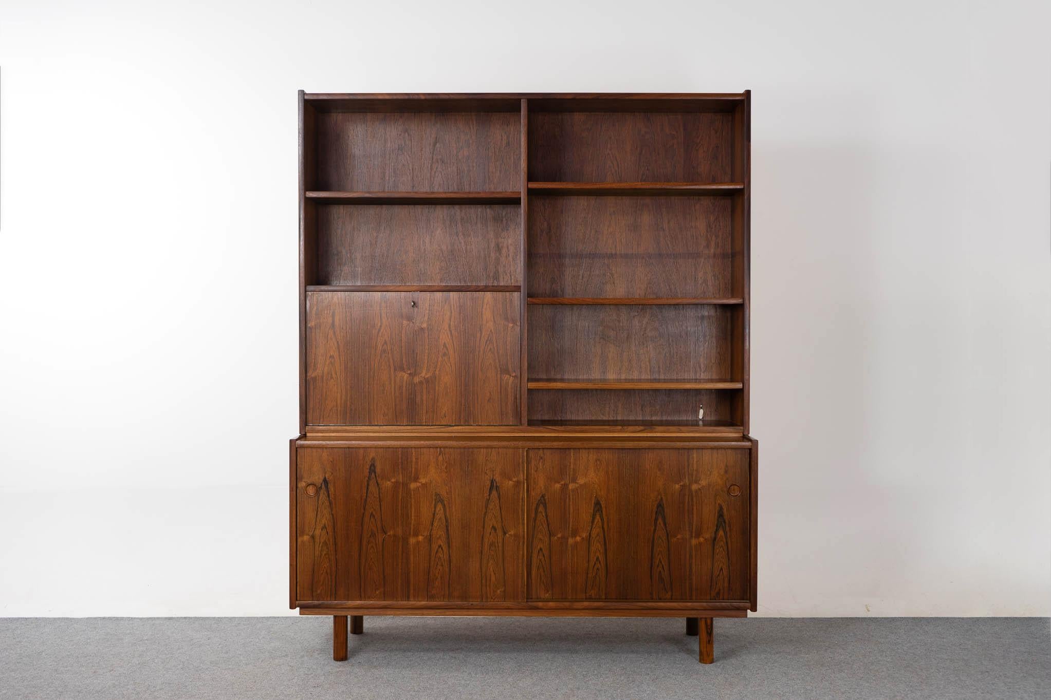 Rosewood Danish modern bookcase/cabinet, circa 1960's. Open bookcase and drop down desk with fitted interior. Lower section with sliding door cabinet, adjustable shelving and slim, sleek drawers. Bookcase rests upon lower cabinet, can be used