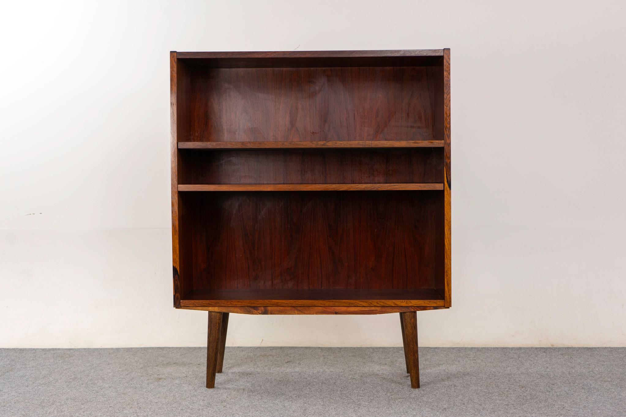 Rosewood bookcase, circa 1960's. Sleek, low profile bookcase with bookmatched veneer, splayed tapered legs and 2 adjustable shelves. 

Unrestored item with the option to purchase restored for an additional $200 USD. Restoration includes: repairs,