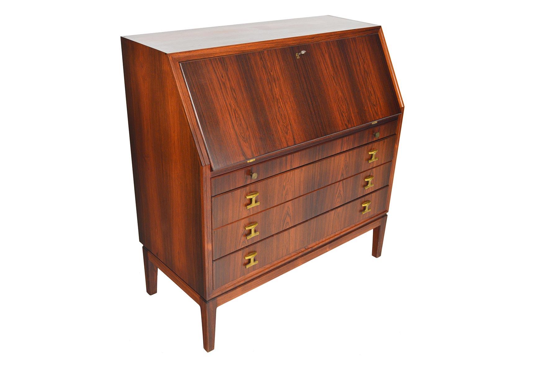 This beautifully appointed Danish modern rosewood secretary desk features rich grain and spectacular original brass hardware. Cased with a mitered joinery and beveled edge, a large desk surface is revealed when the door is lowered. The interior