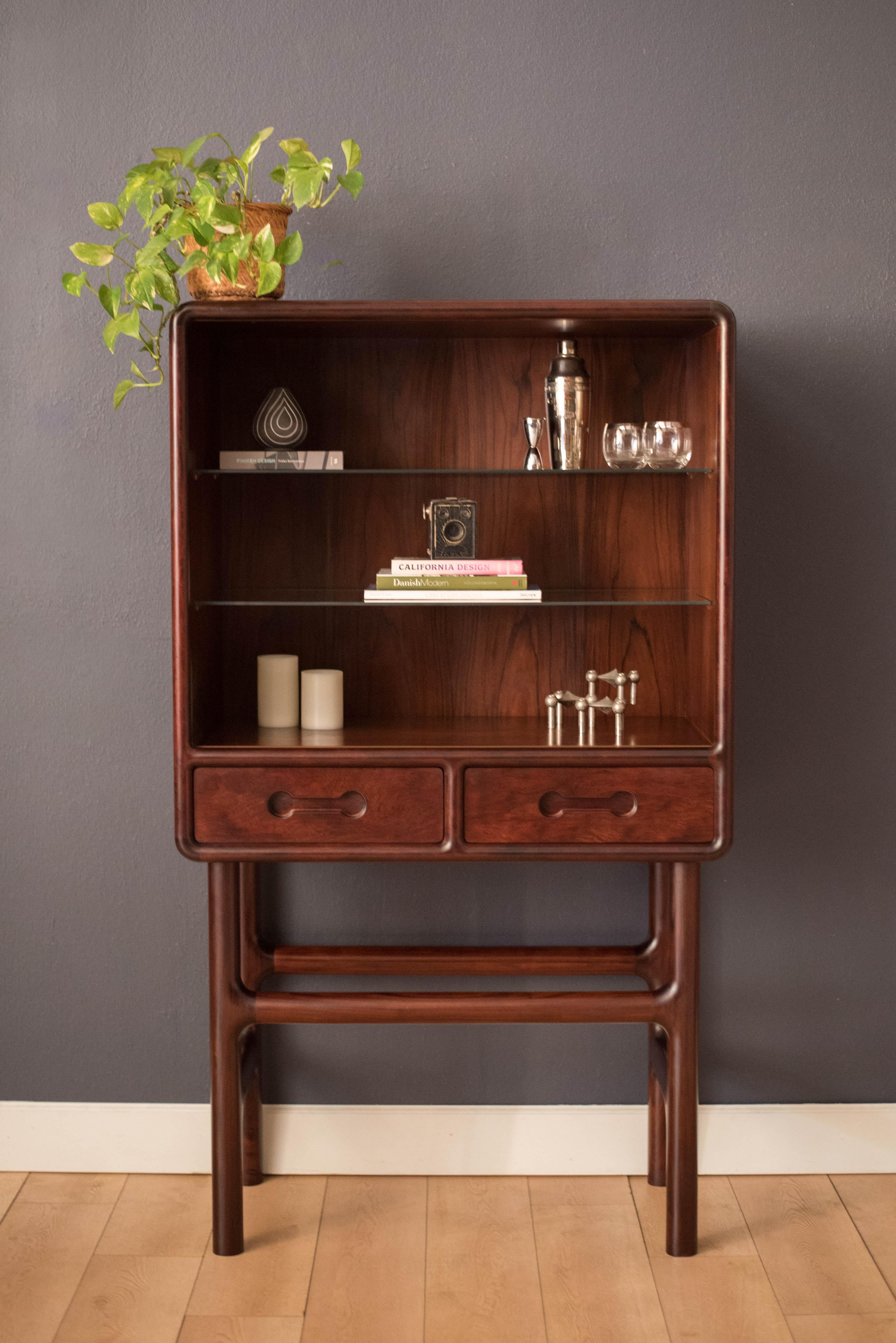 Mid-Century Modern cocktail dry bar cabinet in rosewood made in Denmark circa 1970's. This unique storage piece features a curvilinear profile and a tall supporting base. Includes two buffet drawers with sculptural inset handles and two adjustable