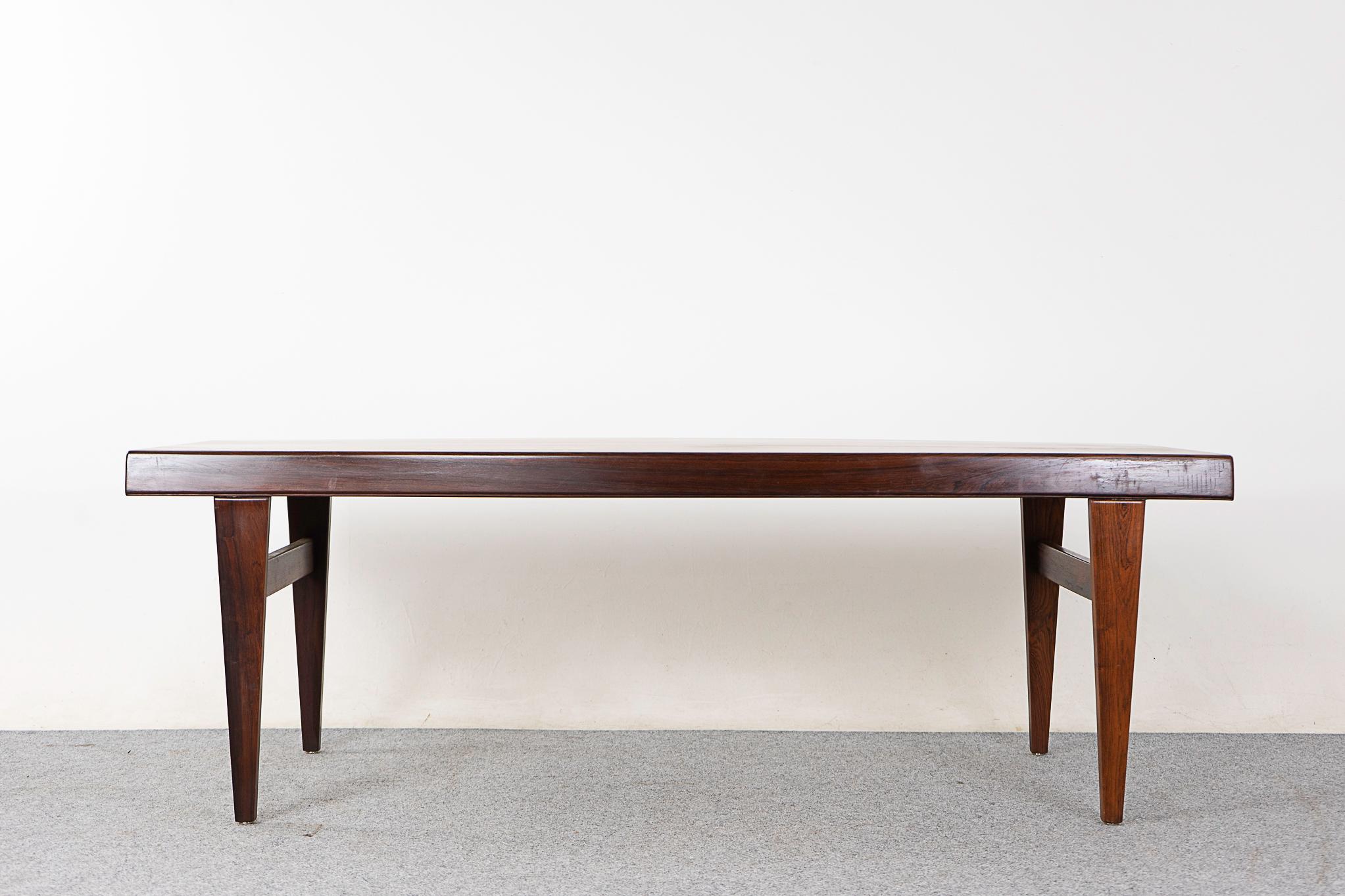Rosewood mid-century coffee table, circa 1960's. Top surface has beautiful book matched veneer and solid wood curved edge along its length. Conveniently concealed moisture resistant pull out extension on one side, on the other a handy drawer, hide