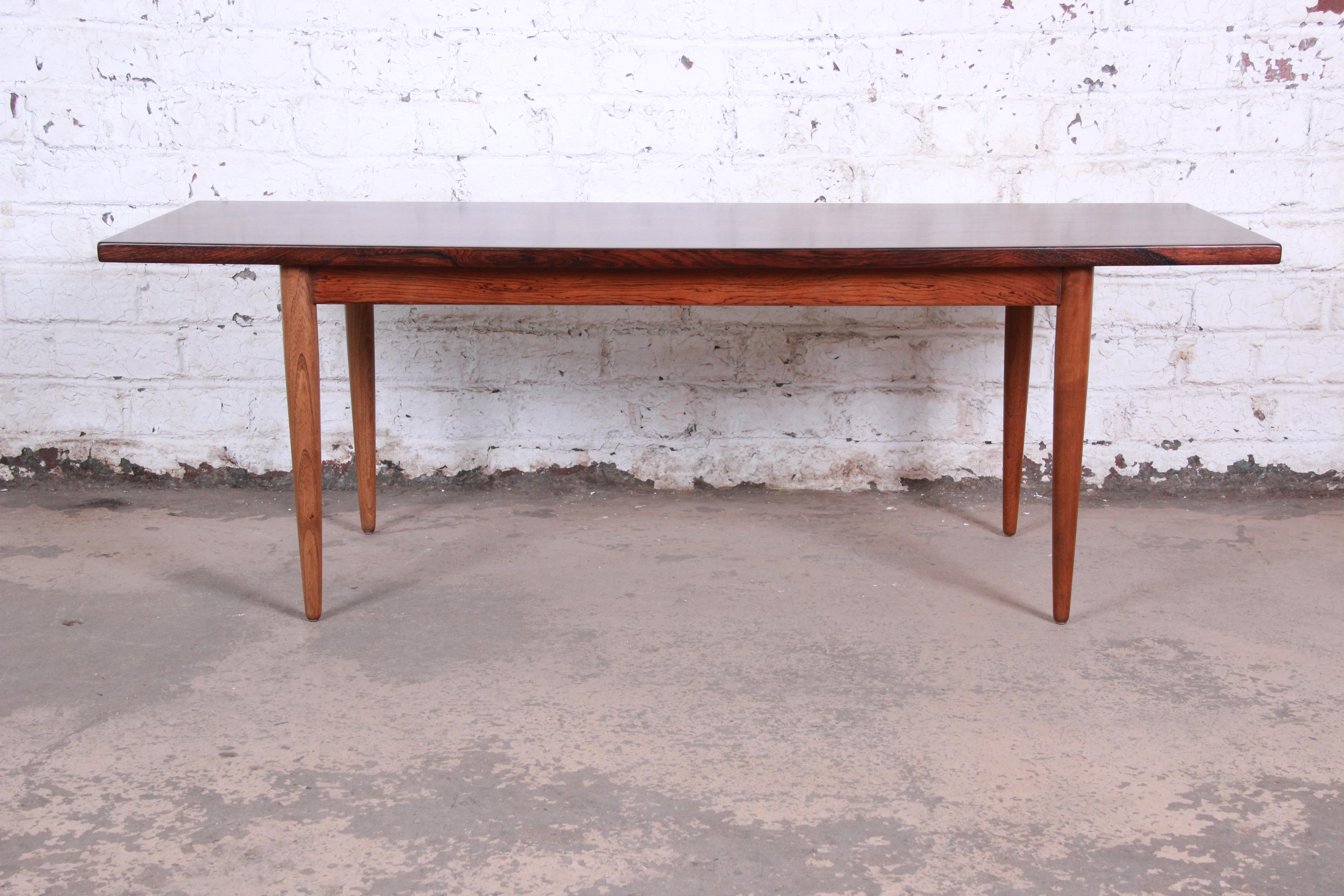 A stunning midcentury Danish modern rosewood coffee table in the manner of Johannes Andersen. The table features stunning rosewood grain and sleek, Minimalist Danish design. It is newly refinished and is in excellent condition.