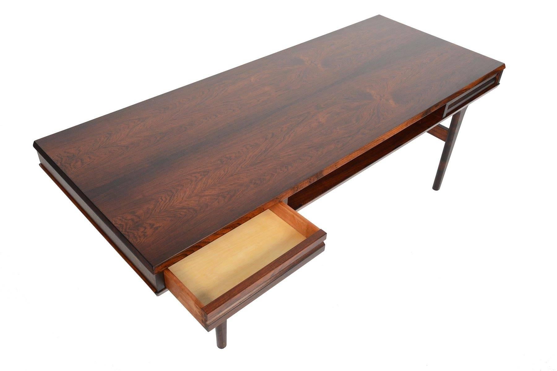 This Danish modern coffee table in rosewood is designed with handsome lines and offers exceptional storage! Beneath a large slab of bookmatched rosewood, sits two drawers that can be opened from either side of the table. A spacious cubby sits in the