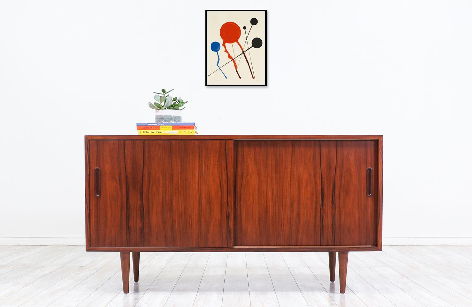 Elegant modern credenza designed by Carlo Jensen for Hundevad & Co. in Denmark circa 1960s. This compact credenza features an exotic rosewood grain detail and a sturdy construction sitting on four classic tapered legs. Behind the sliding doors, they