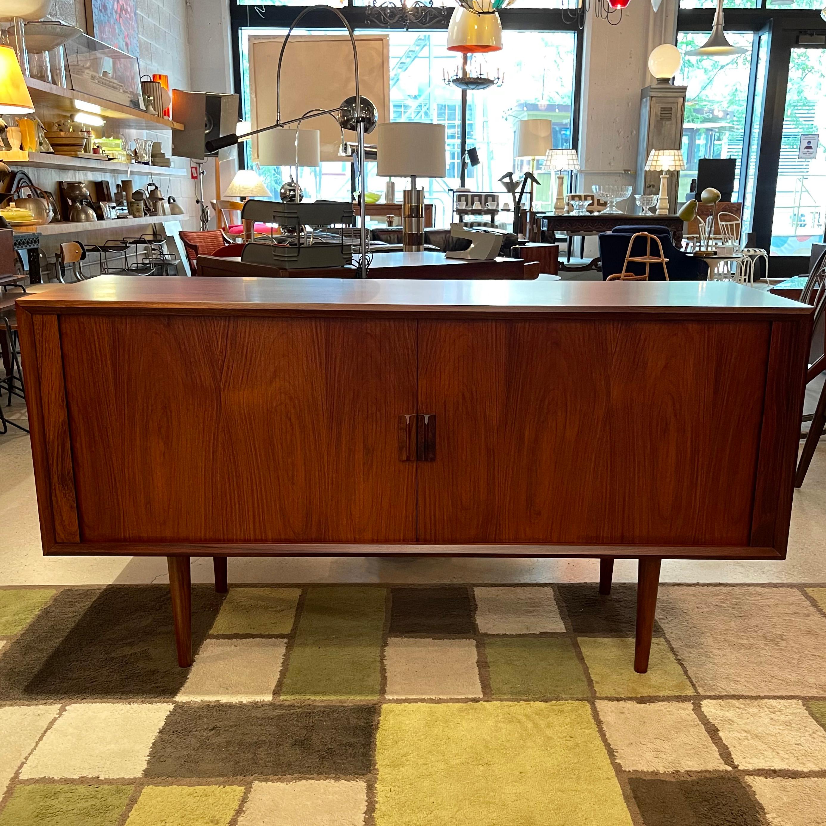 Danish modern, rosewood credenza by Svend Aage Larsen for Faarup Mobelfabrik features a tambour front with interior shelves and pull-out drawers. The credenza is nicely sized at 59 inches wide and finshed on the back so it can float in a room.
