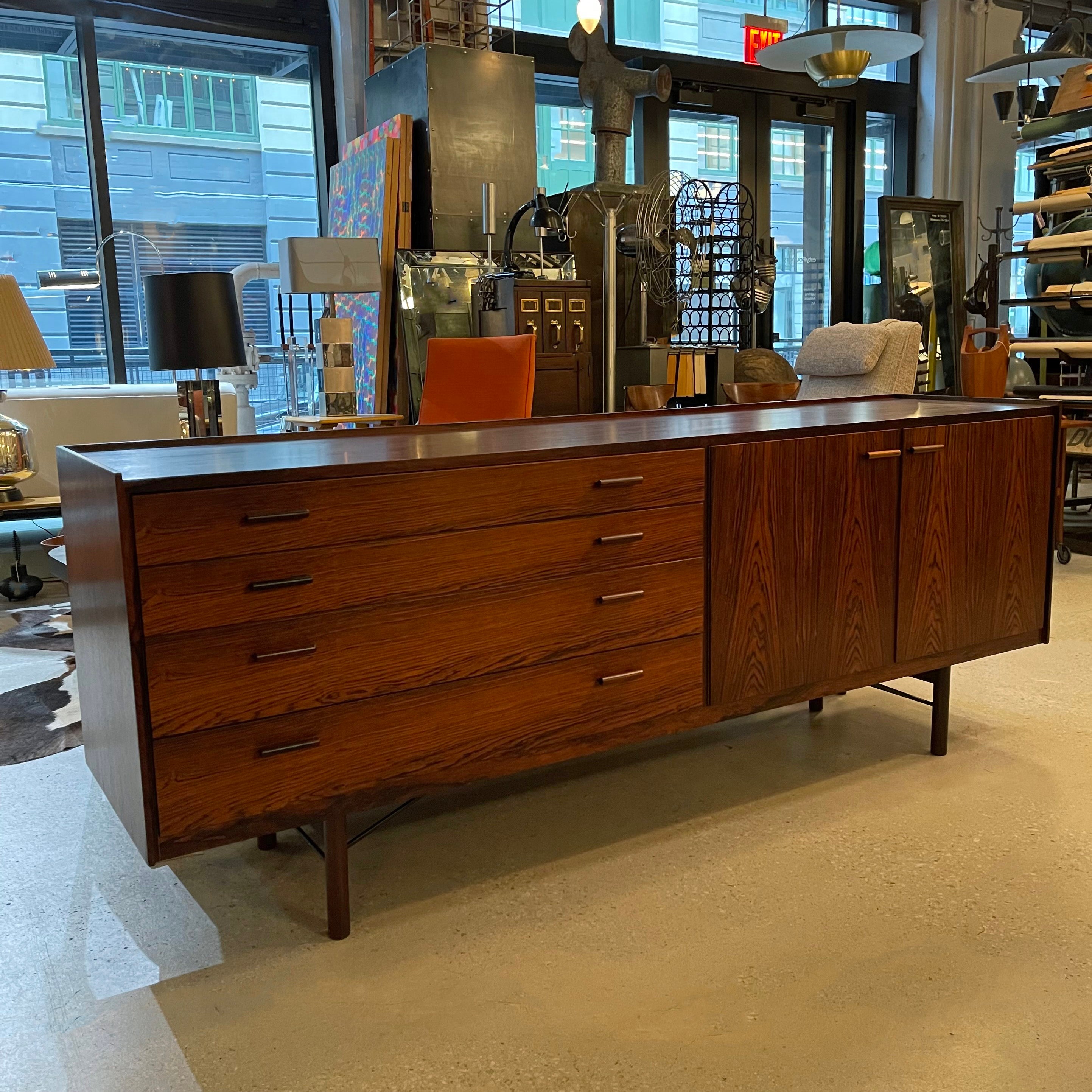Mid-century, Danish modern, rosewood credenza sideboard features a rich tone and wonderful grain throughout with streamilned, linear pulls. It offers a great deal of storage with 4 drawers on one side and pull-out and stationary shelves on the