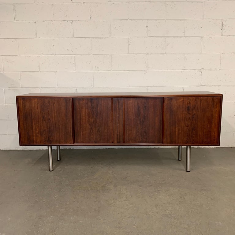 Sleek and minimal, Danish modern credenza / sideboard features a beautiful grain, rosewood body with sliding doors, atop tubular chrome legs. The interior features 2 inside drawers and shelving.