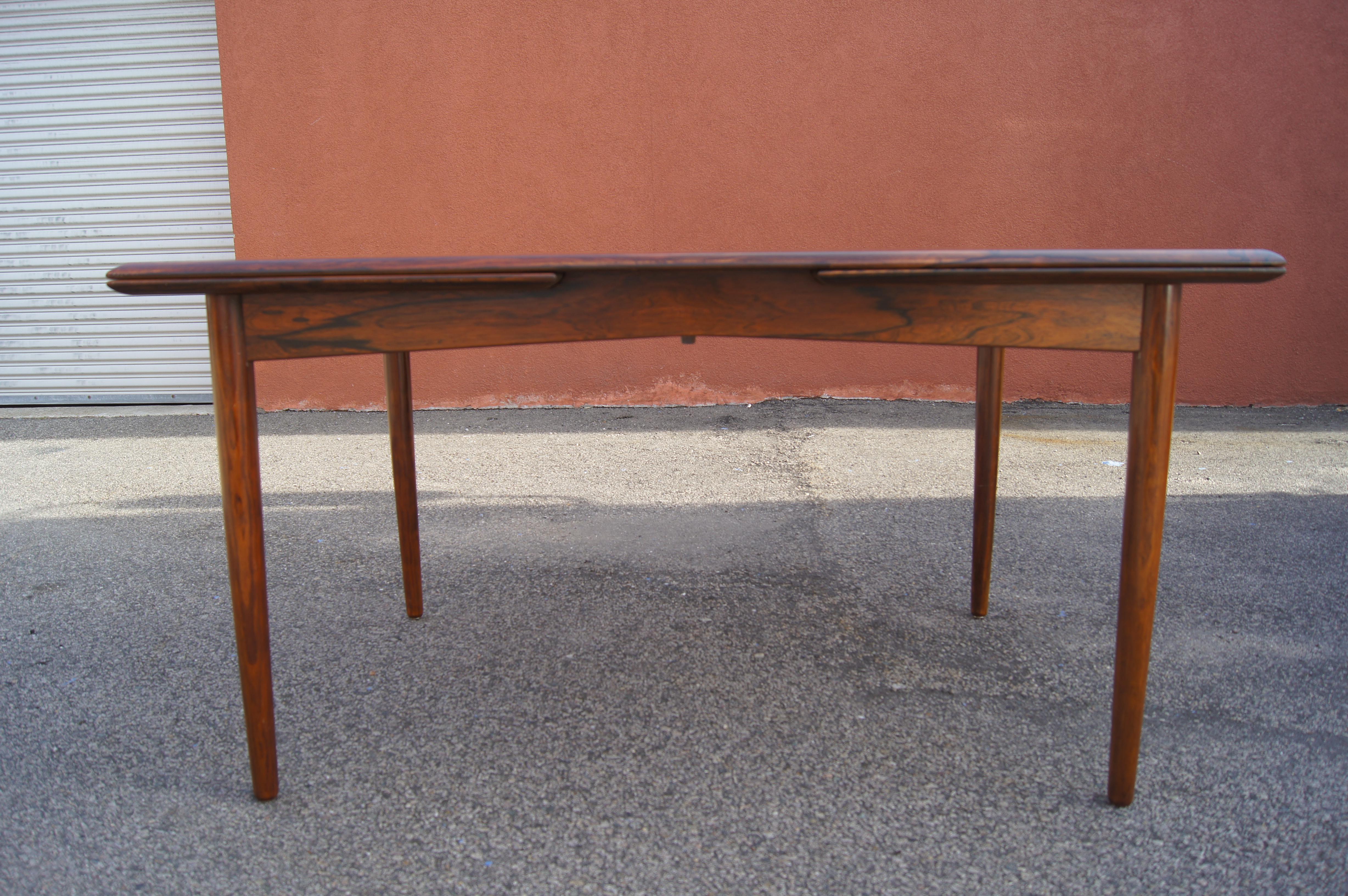 Esta mesa de comedor de palisandro es un maravilloso ejemplo del modernismo danés, que equilibra líneas limpias y una riqueza orgánica. Apoyado sobre esbeltas patas cónicas, el tablero de vivo veteado oculta dos hojas interiores de 21,5 pulgadas que