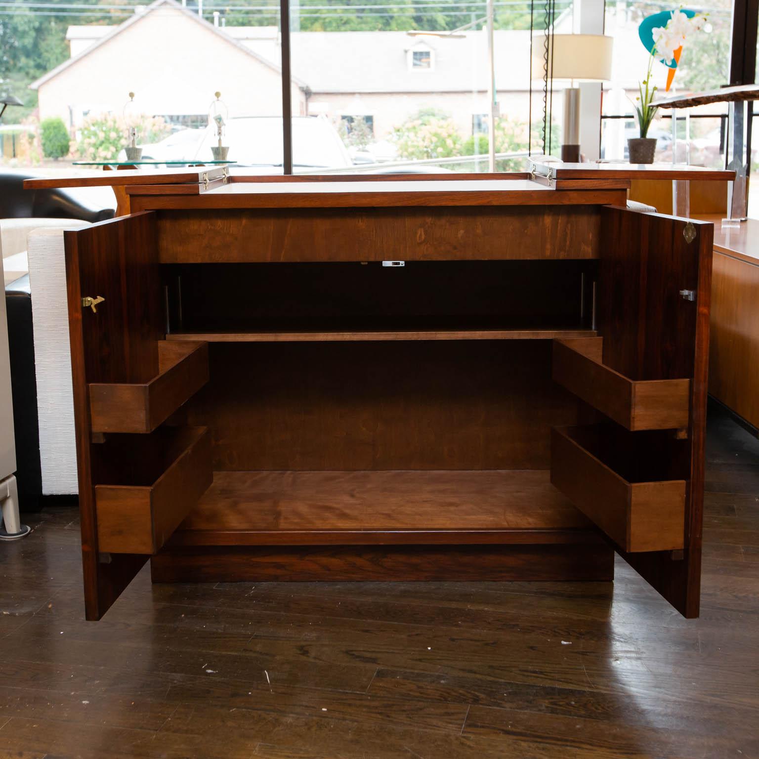Restored mid-Century Modern rosewood bar cabinet with white formica deck hidden under its book matched rosewood outer veneer. Center well for ice or drink preparation. Shelves on doors for liquor bottles and glasses. Lock does not have key. Open the