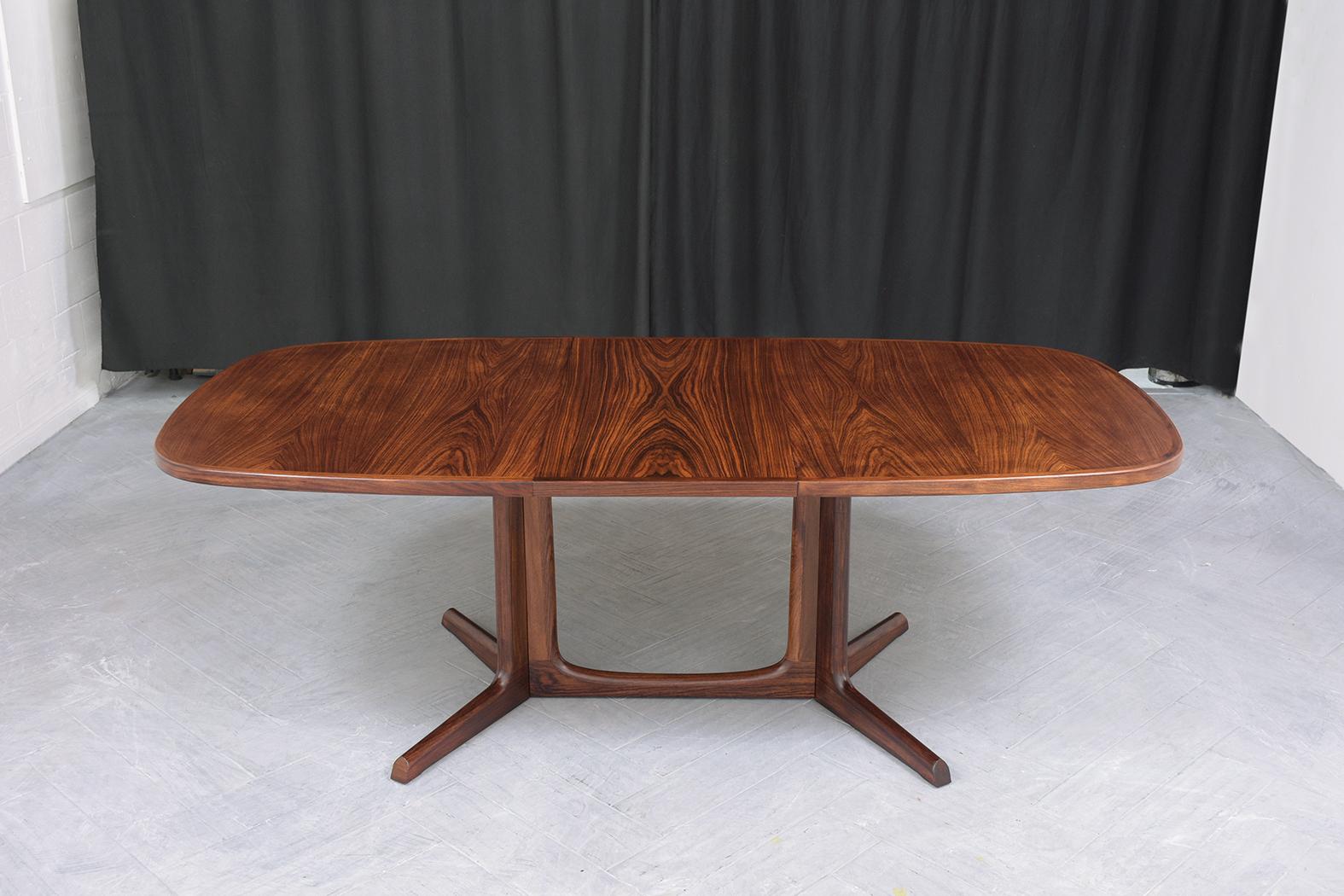 This extraordinary vintage mid-century dining table is in excellent condition and is hand-crafted out of beautiful rosewood and professionally restored by our expert craftsman team. This 1960s danish dining room table features eye-catching mahogany