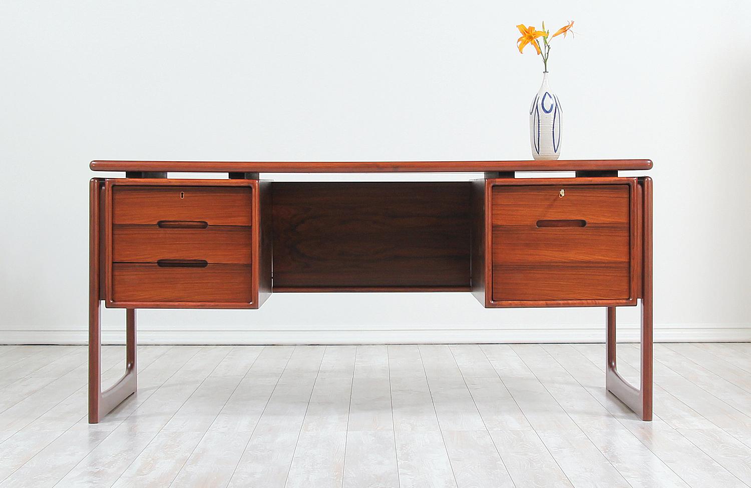 Stylish modern executive desk designed and manufactured in Denmark by Dyrlund, circa 1960s. This striking Danish modern design features a rosewood frame and three spacious drawers on the left side, a file cabinet on the right, and an open back with
