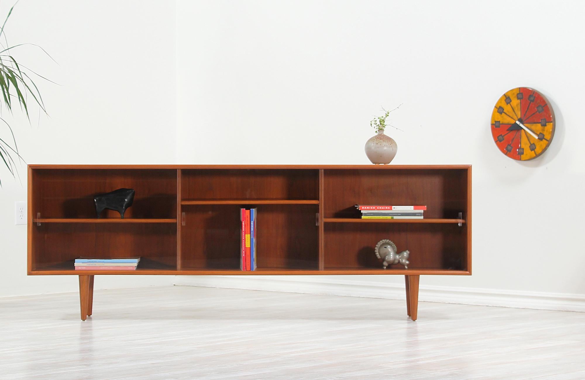 Minimalist Danish modern bookcase designed and manufactured by H.P. Hansen Møbelindustri in Denmark circa 1960s. This sleek design features a sturdy teak case sitting on four tapered legs with its original sliding glass doors. The interior is